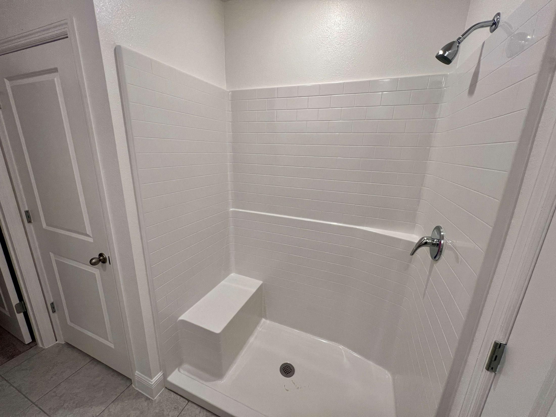 Modern, white tiled walk-in shower with a built-in bench and chrome fixtures.