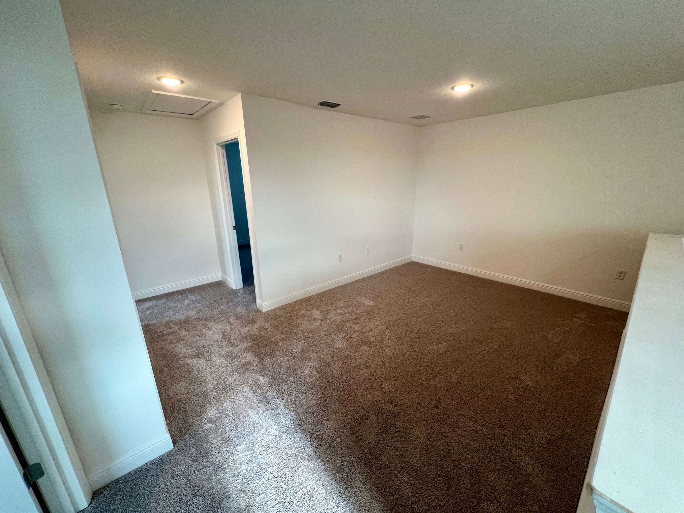 Empty room with beige carpet, white walls, ceiling lights, and an open doorway.