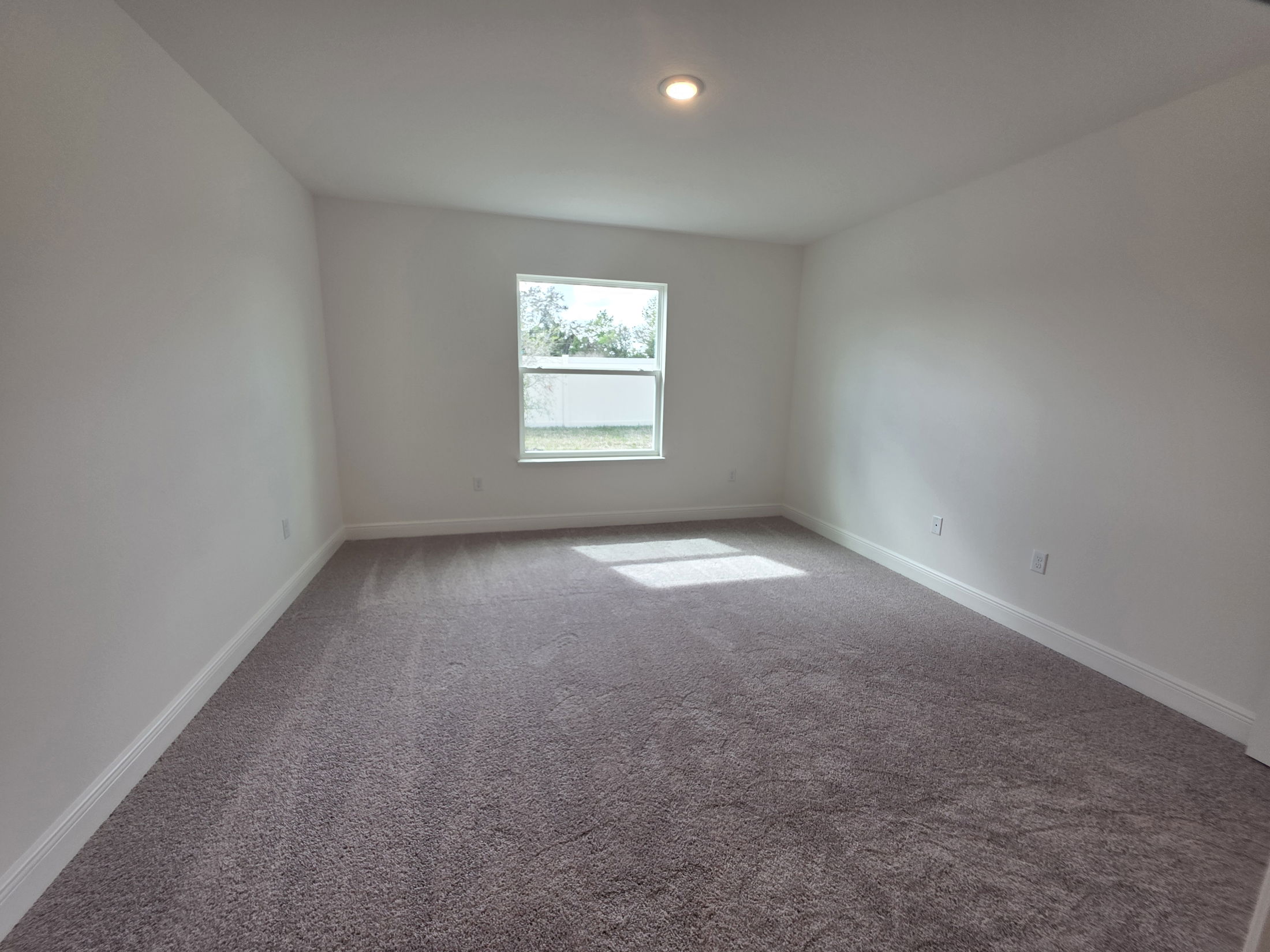 Spacious and bright empty room with light gray carpet and a large window reflecting natural light.