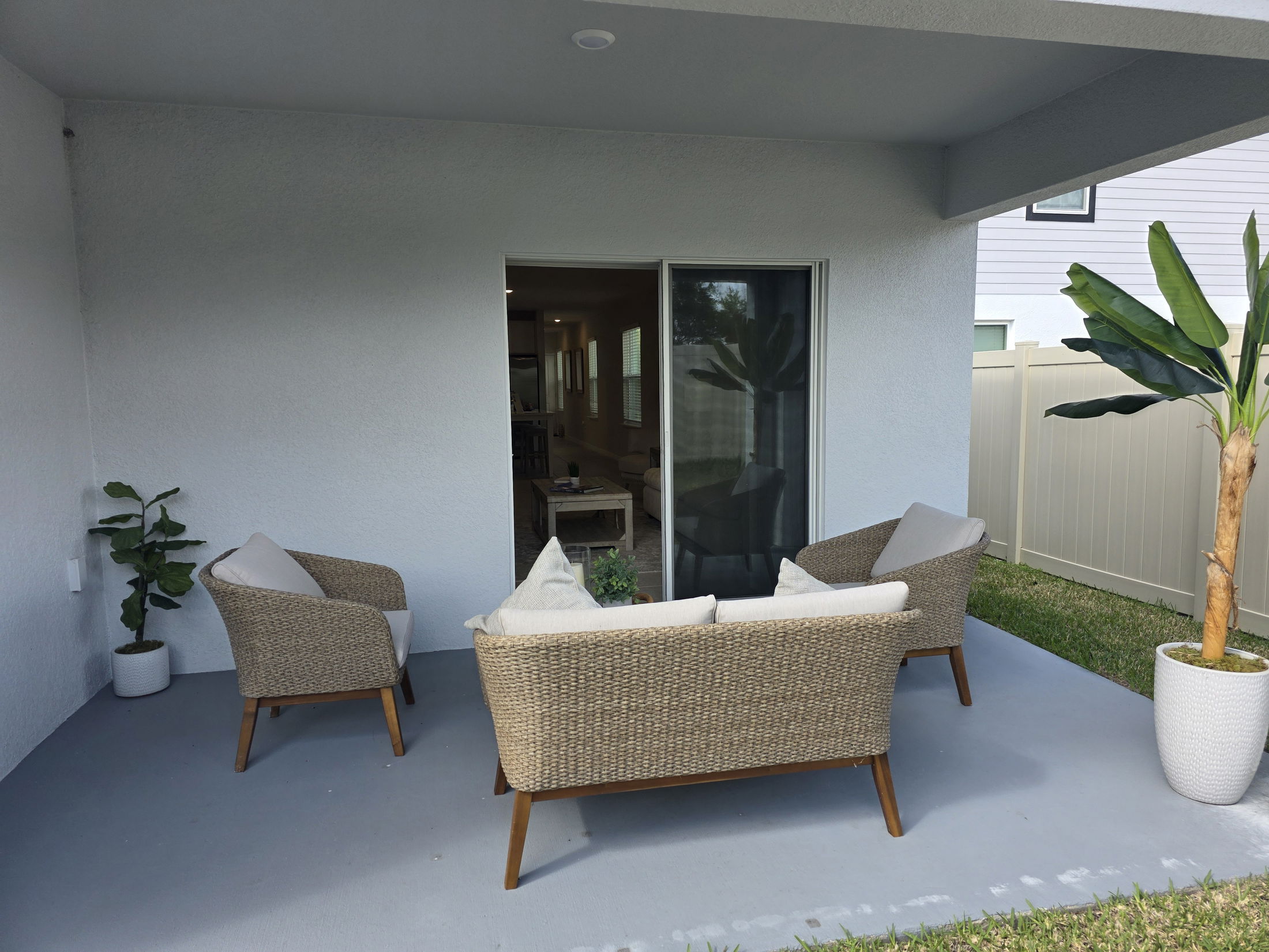 Cozy outdoor patio featuring two wicker chairs with cushions and a potted plant beside a sliding glass door.