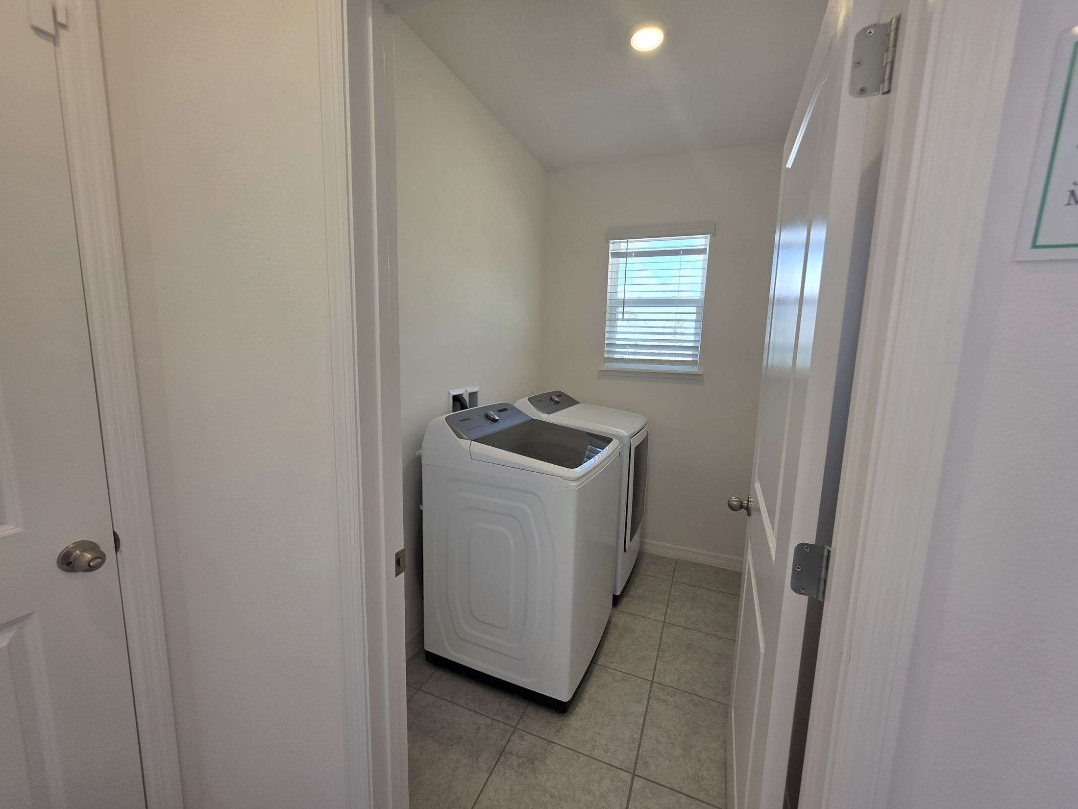 A modern laundry room featuring white washers and dryers in a bright, tiled space with natural light.