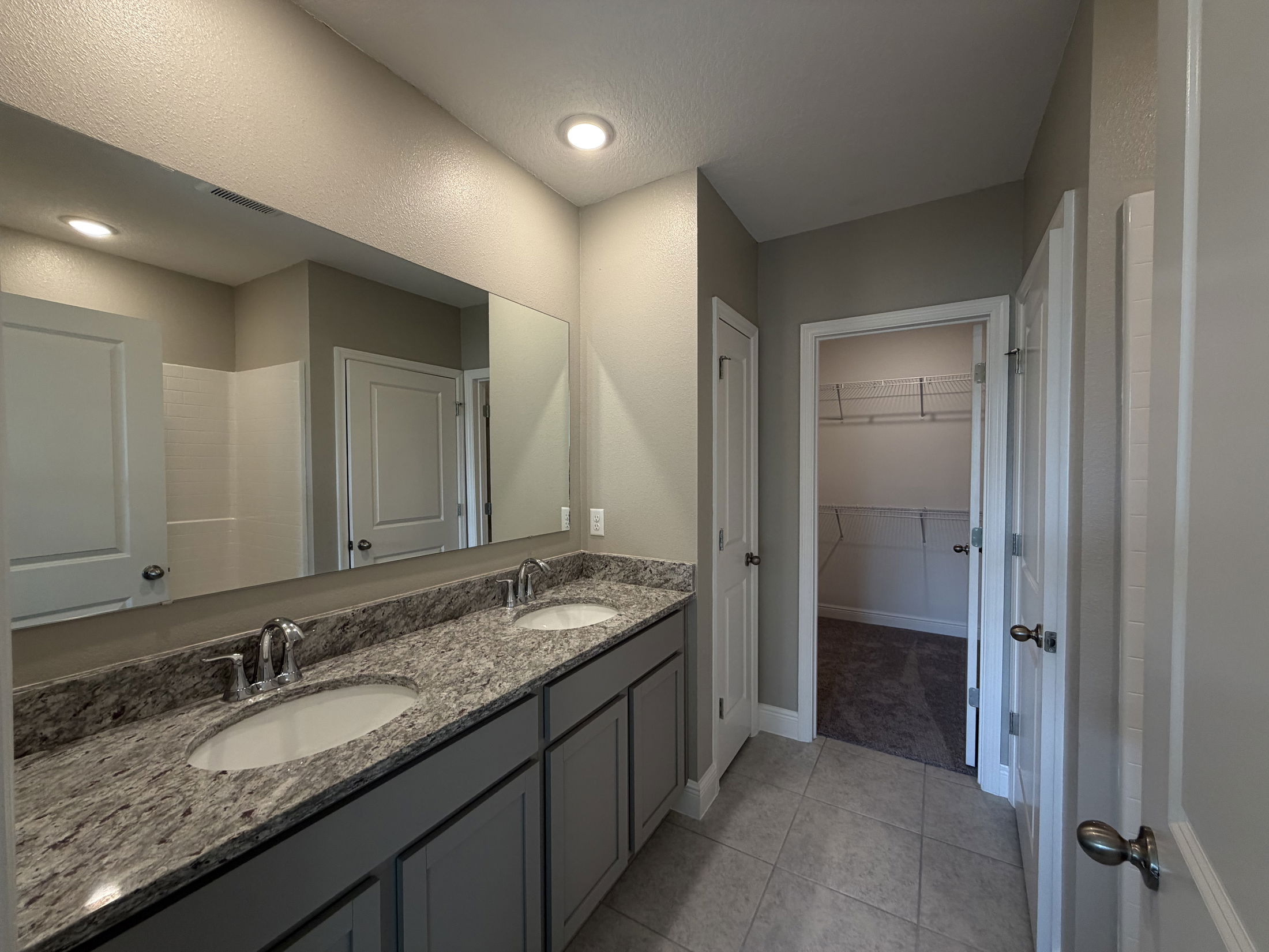Modern bathroom with double vanity, granite counter, and spacious closet access.