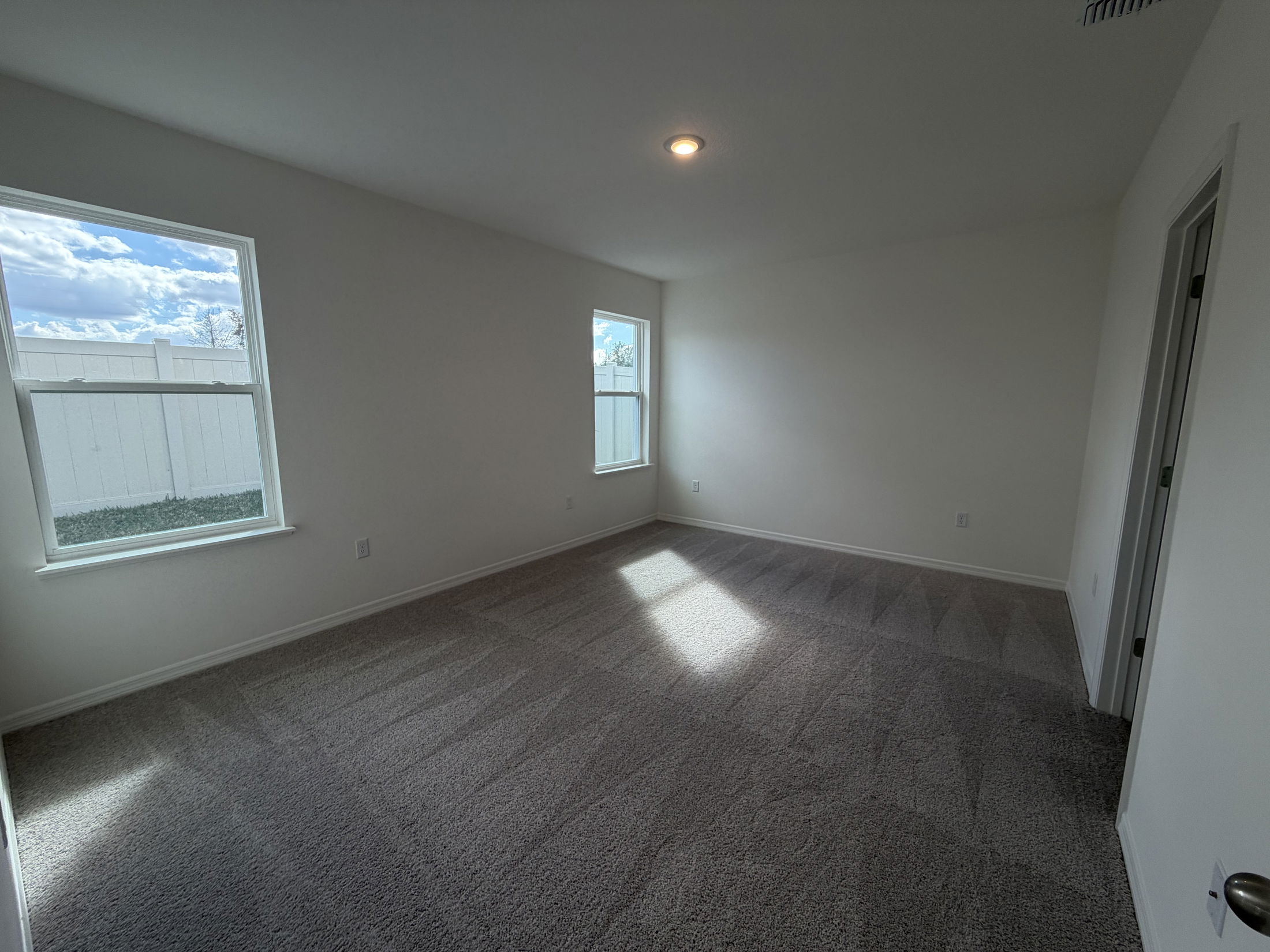 Spacious, well-lit empty bedroom with carpet flooring and two windows showcasing a bright outdoor view.