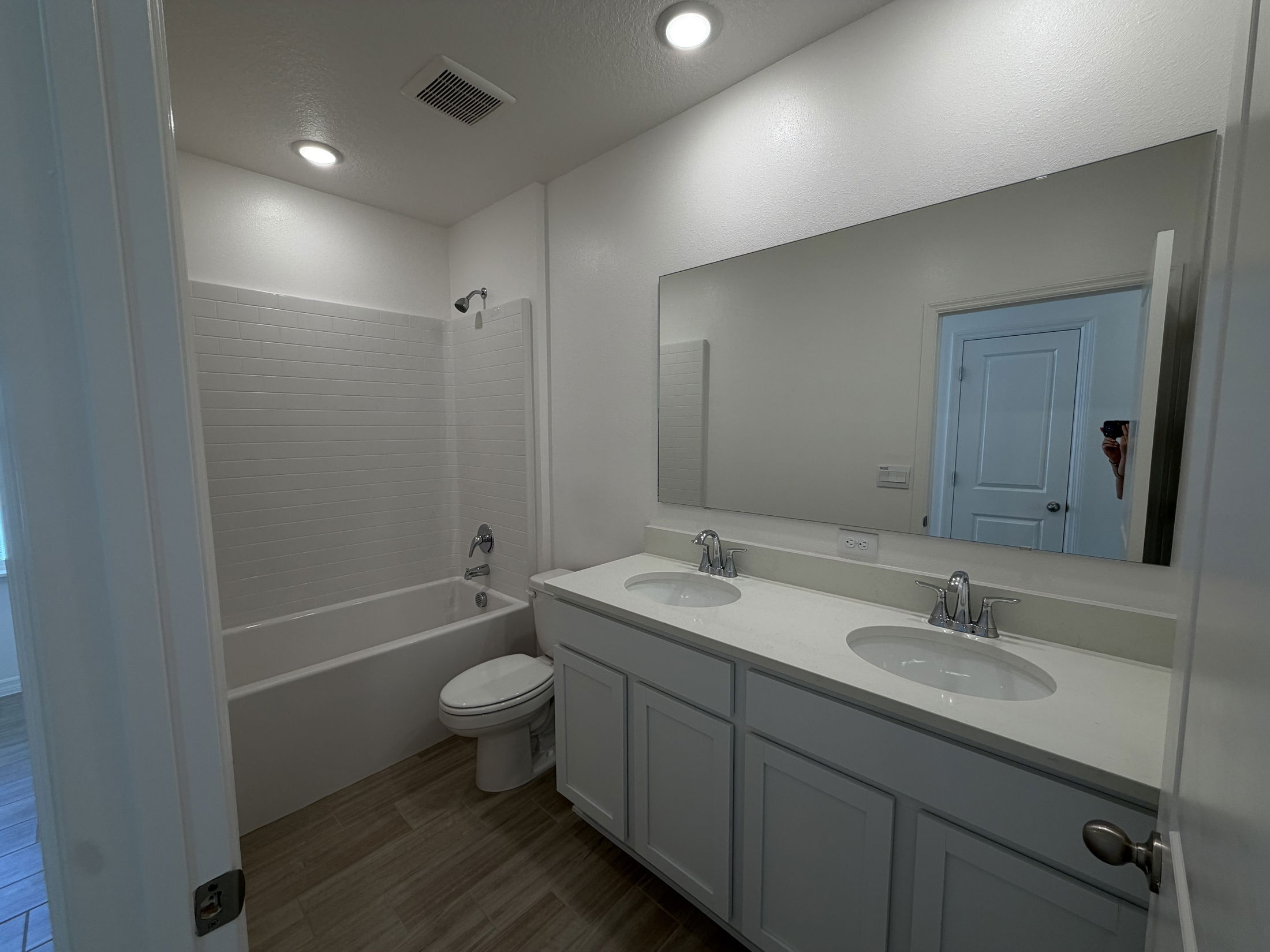 Modern bathroom featuring a white tile shower, double sink vanity with a polished counter, and contemporary lighting.