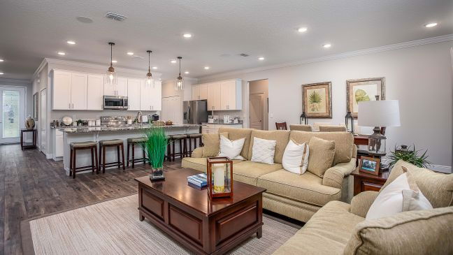 Spacious modern open-concept living room and kitchen with beige sofas, hardwood floors, and stylish lighting.