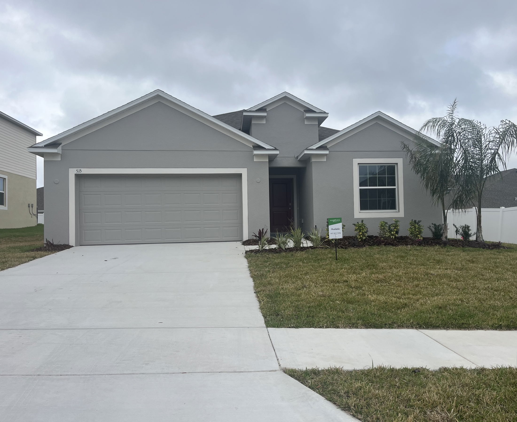 Newly constructed modern grey house with a two-car garage, lush landscaping, and a concrete driveway.