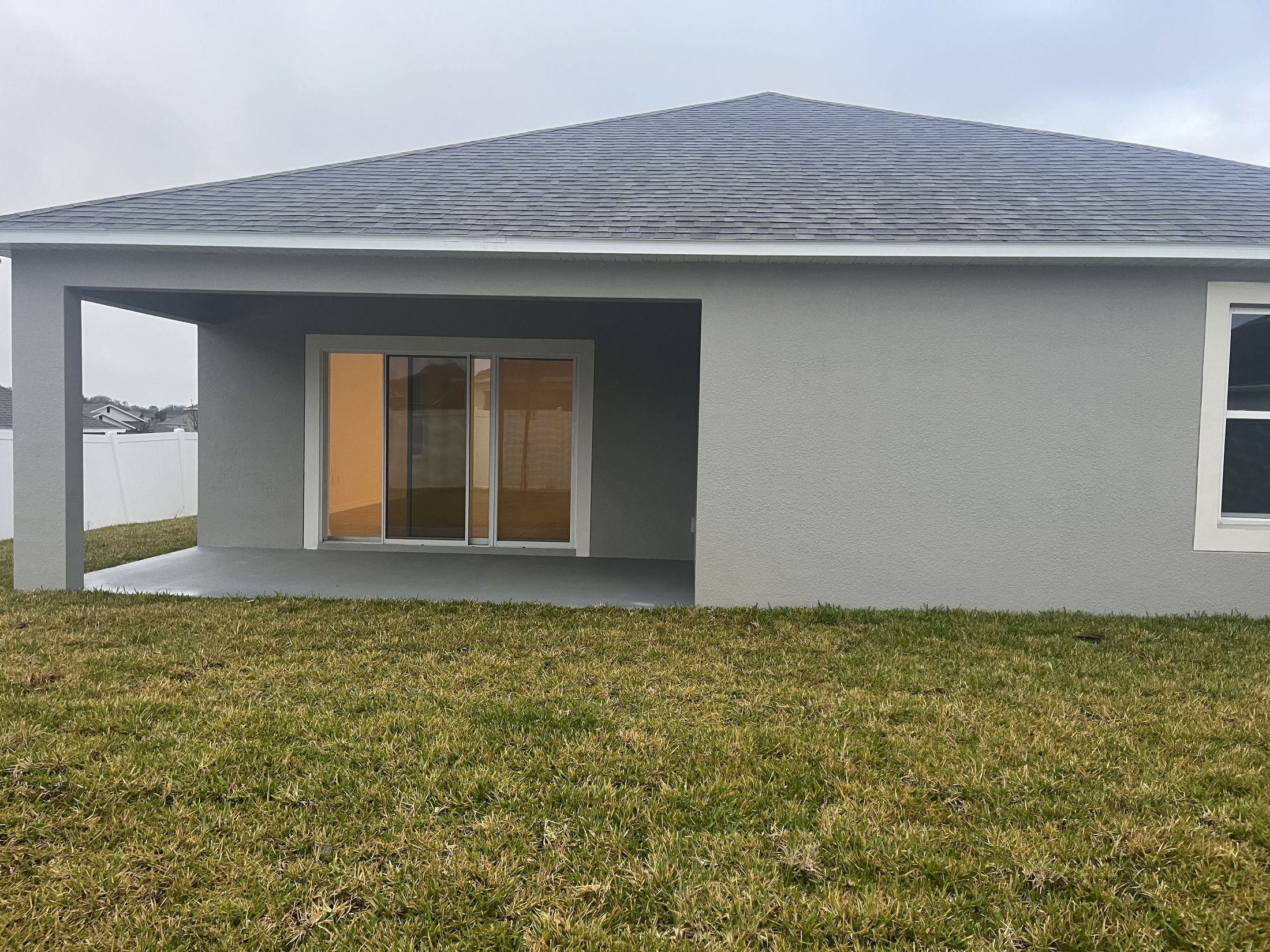 Modern gray house with a covered patio, sliding glass doors, and a grassy backyard.