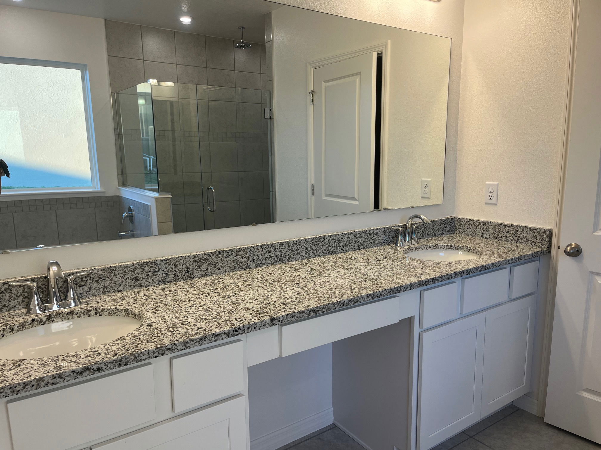 Modern bathroom with granite countertop, dual sinks, large mirror, and glass-enclosed shower.