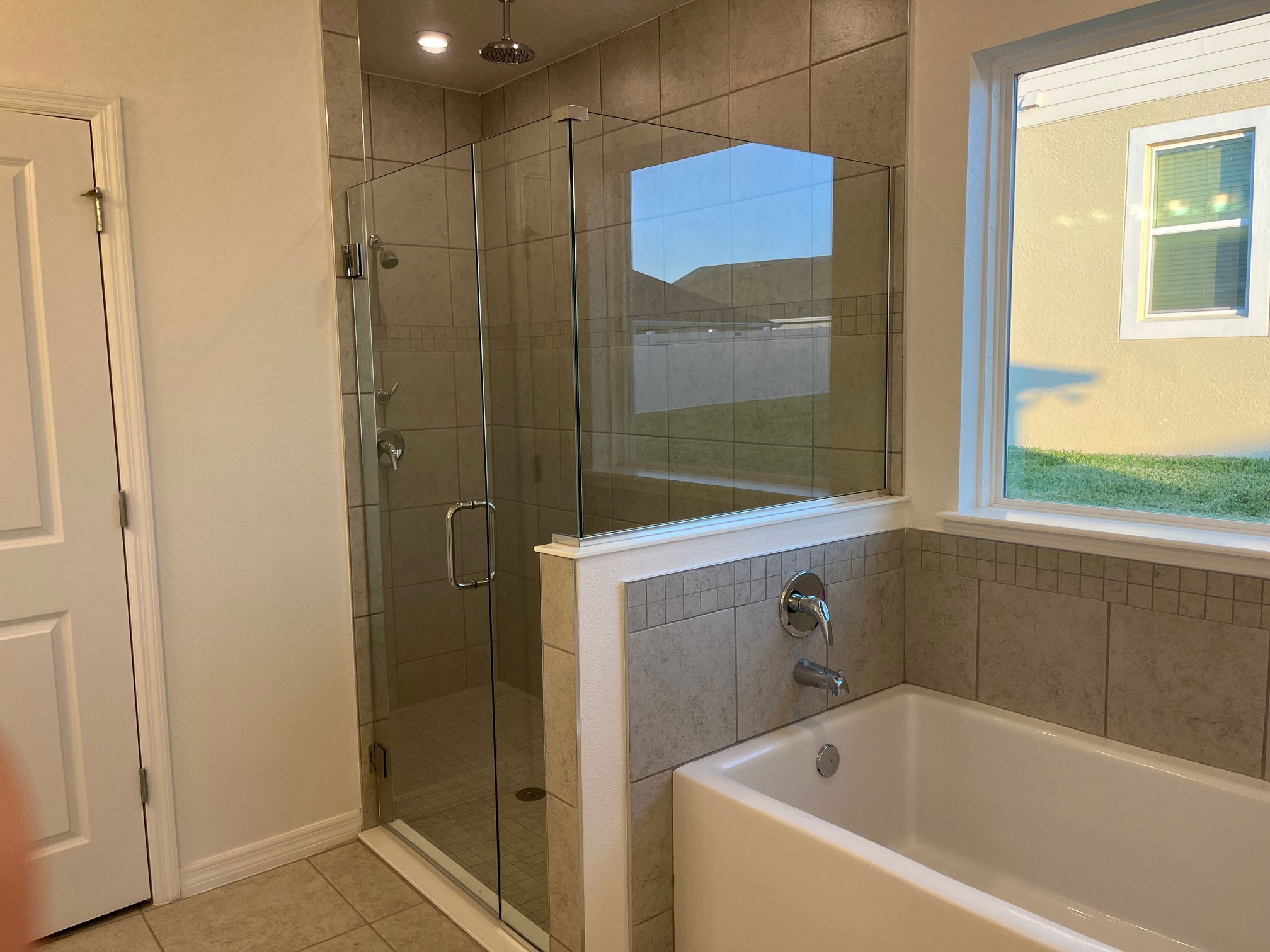 Modern bathroom featuring a glass-enclosed shower and a tiled bathtub next to a window.
