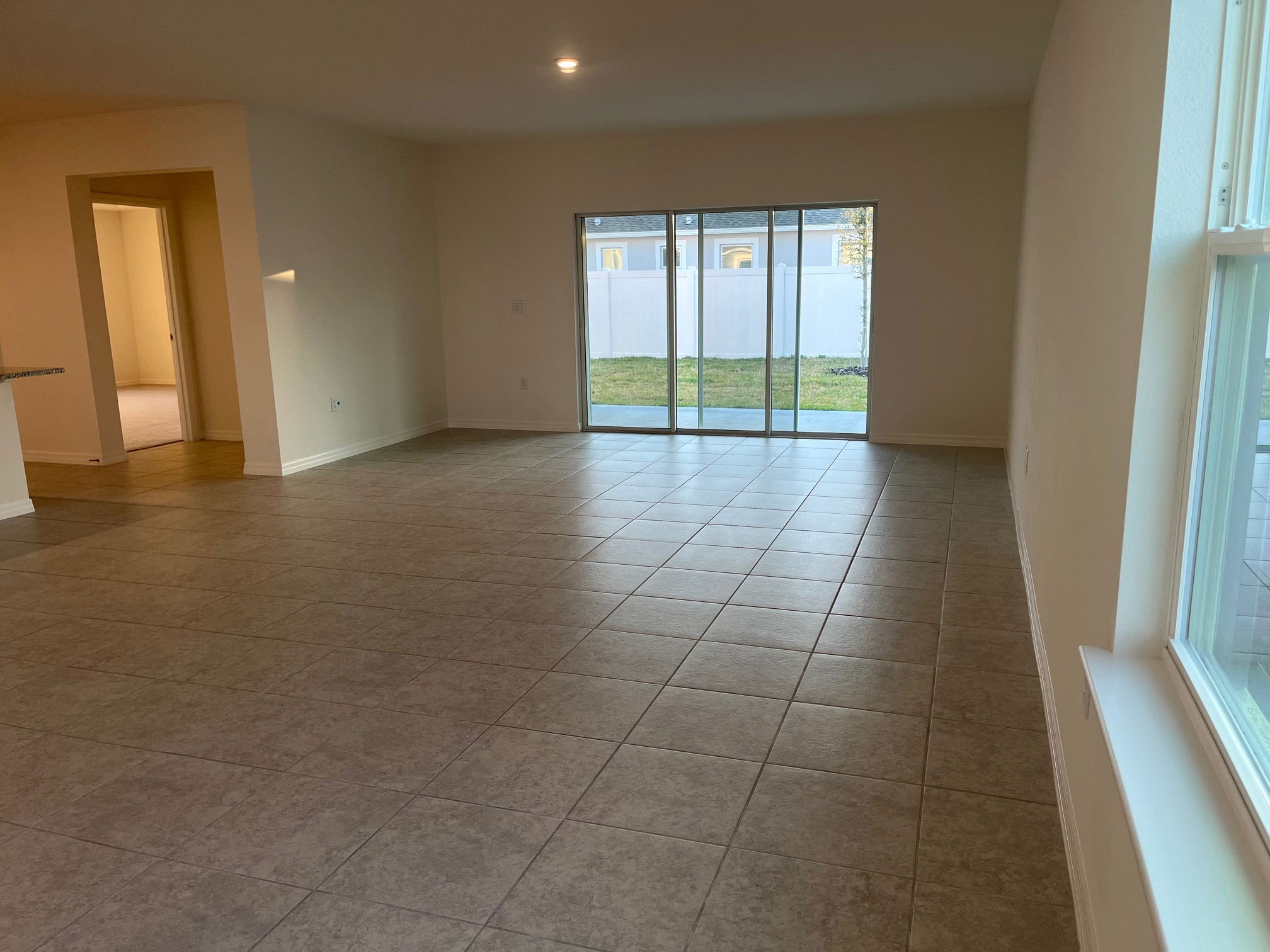 Spacious empty living room with large tiles, sliding glass doors, and a view of the backyard.