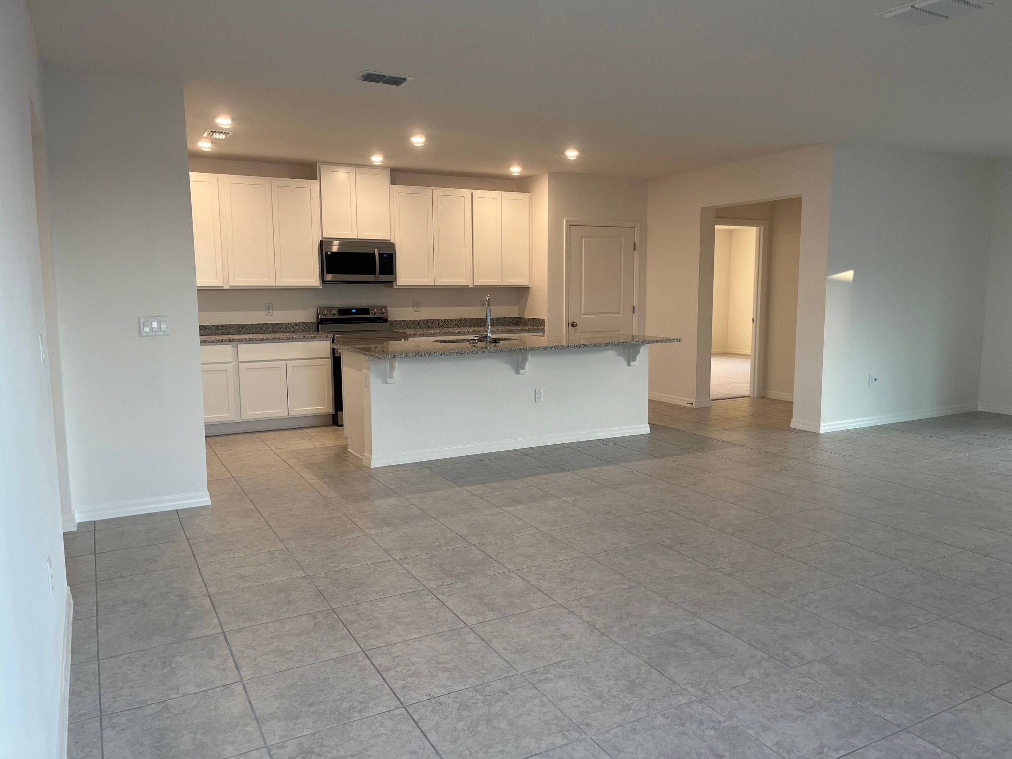Modern open-concept kitchen and living area with tiled floors, white cabinetry, and stainless steel appliances.