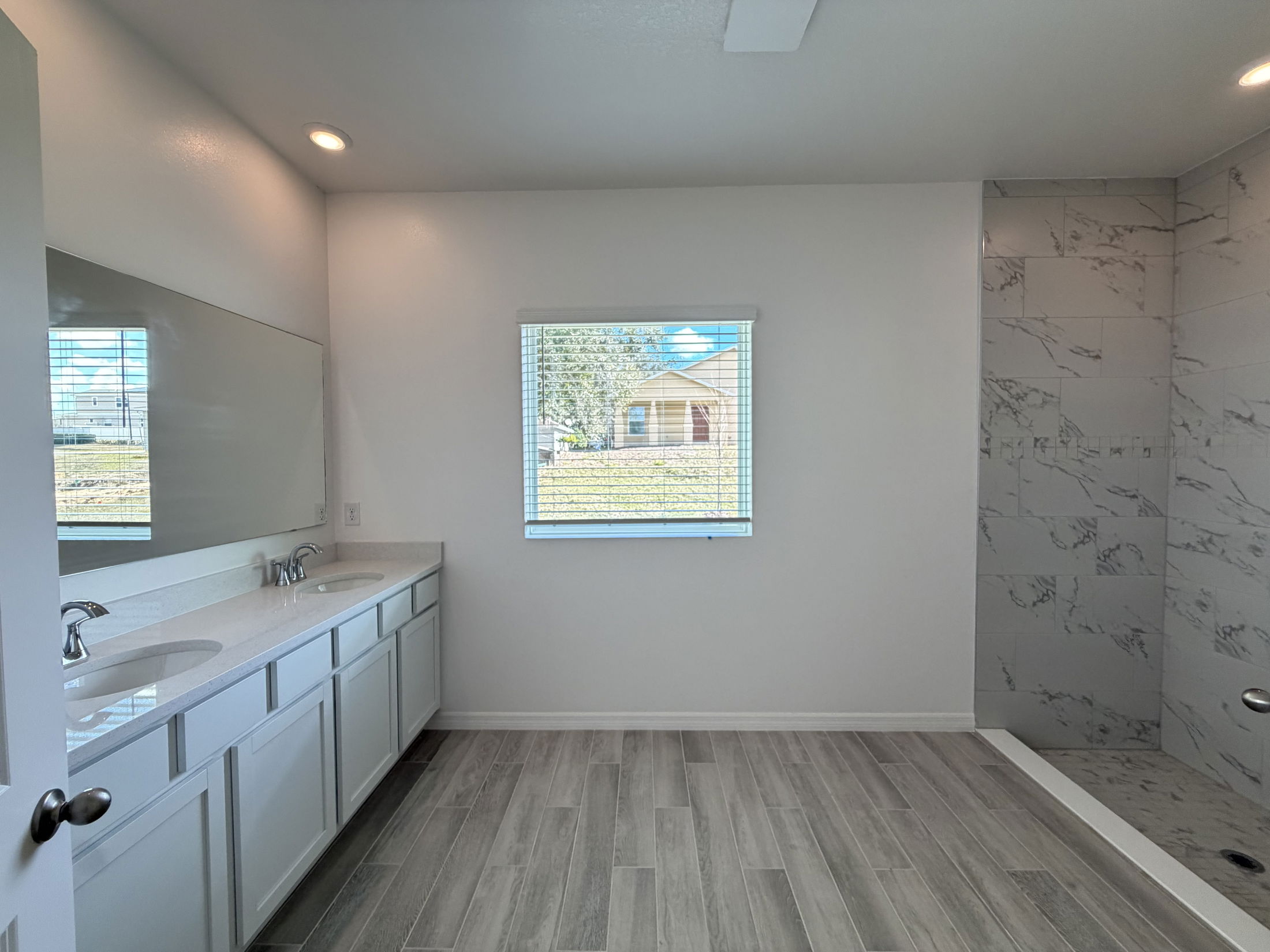 Modern bathroom interior featuring a double sink vanity, large mirror, and a walk-in shower with marble tiles.