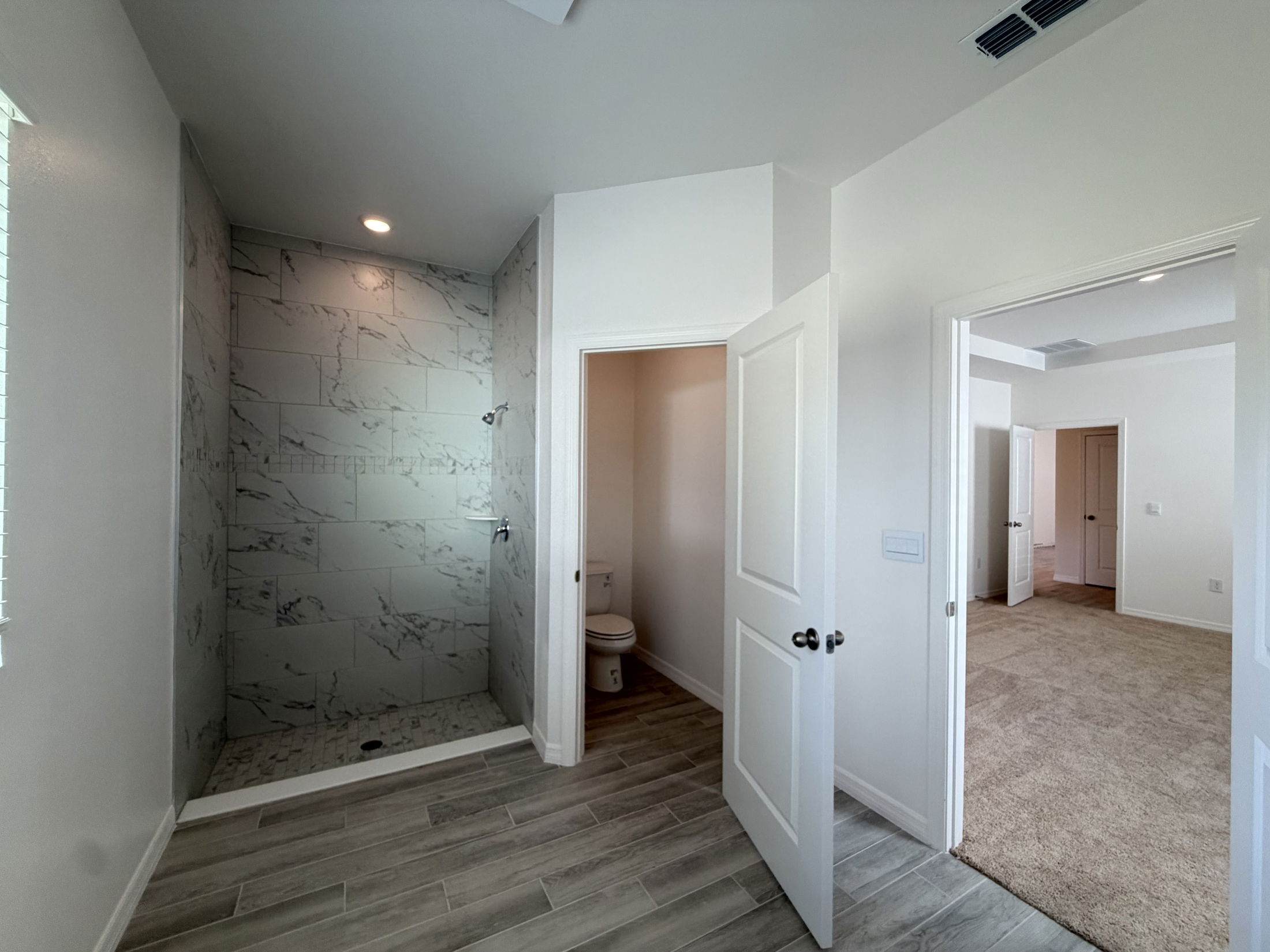 Modern bathroom with marble tiled shower and entry to carpeted bedroom in a newly constructed home.