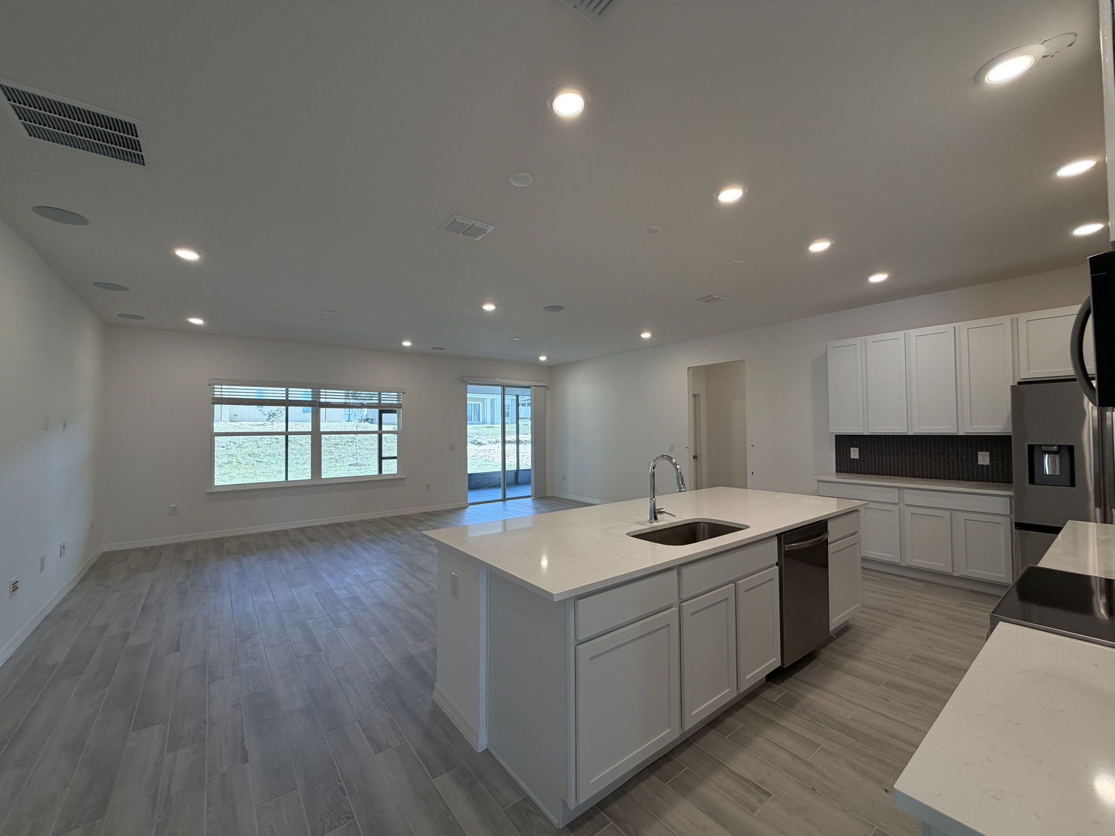 Modern open-concept kitchen and living room with white cabinetry, quartz countertops, and large windows allowing natural light.