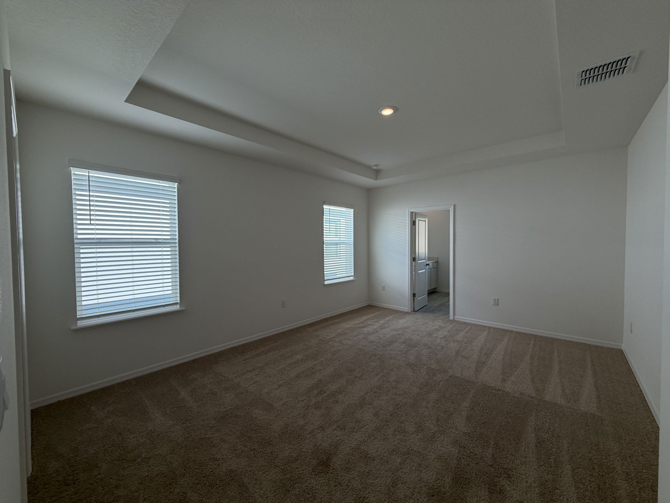 Spacious and well-lit empty bedroom featuring carpet flooring and white walls with windows offering natural light.