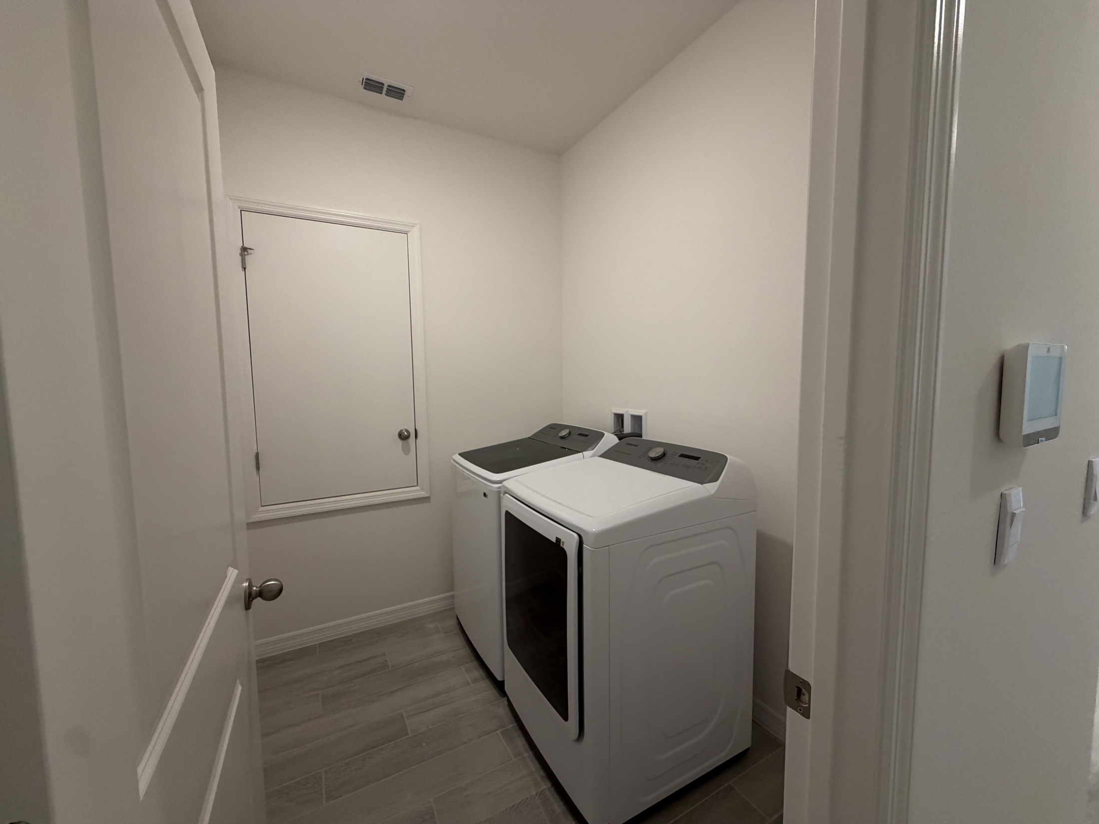 A modern laundry room featuring stacked white washing machines and a clean, minimalistic design with light-colored walls and tile flooring.