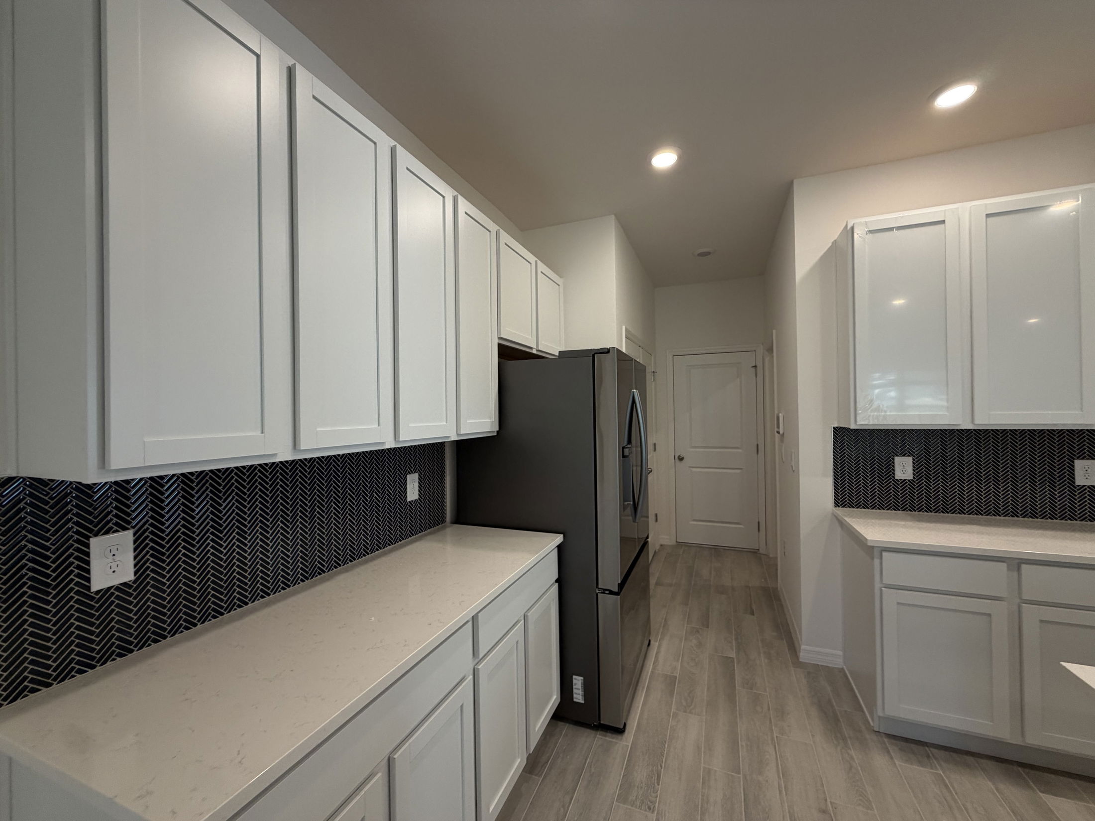Modern kitchen featuring white cabinets, a sleek black herringbone backsplash, and stainless steel appliances.