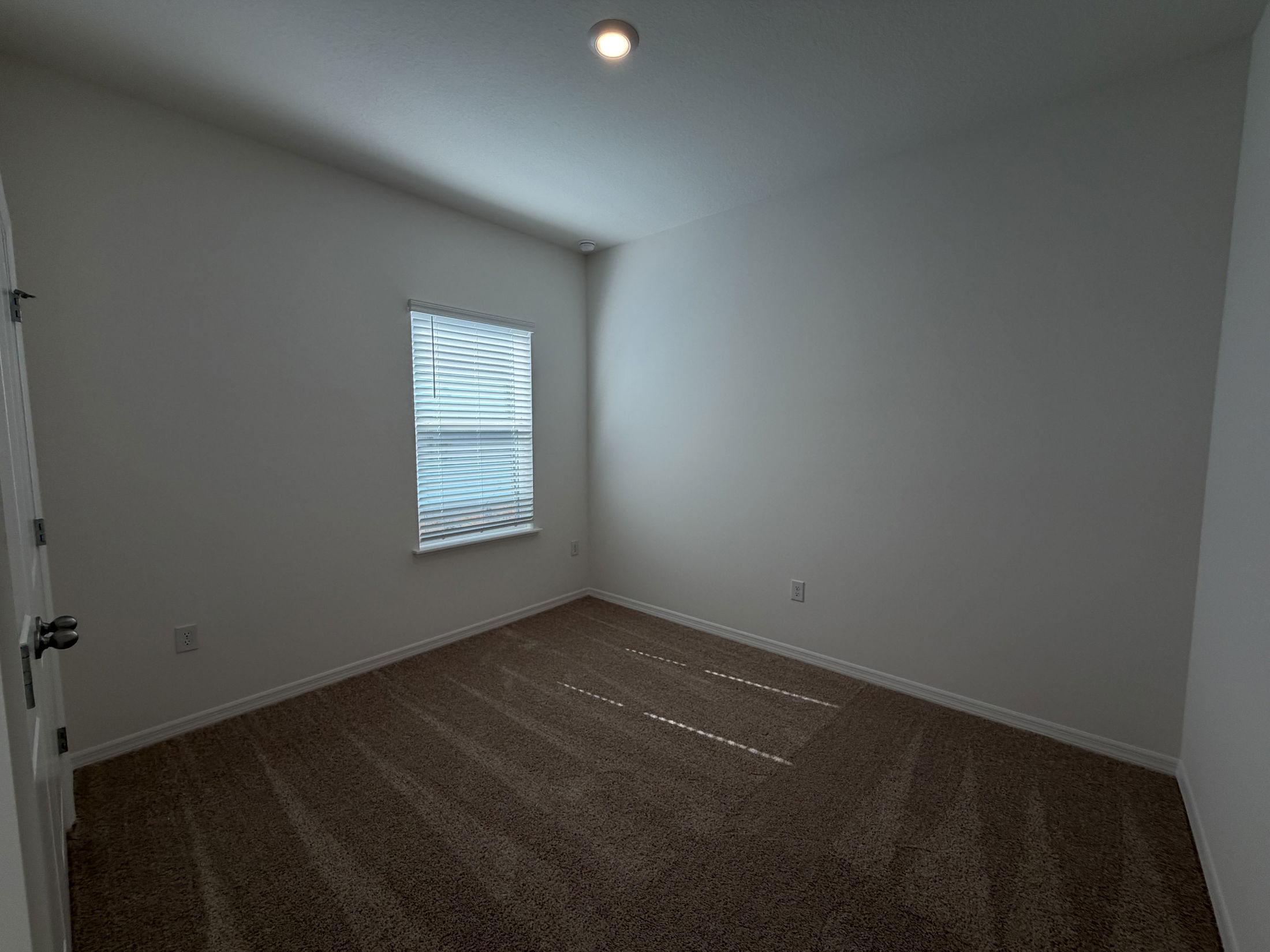 Spacious, empty room with natural light filtering through a window and beige carpet flooring.