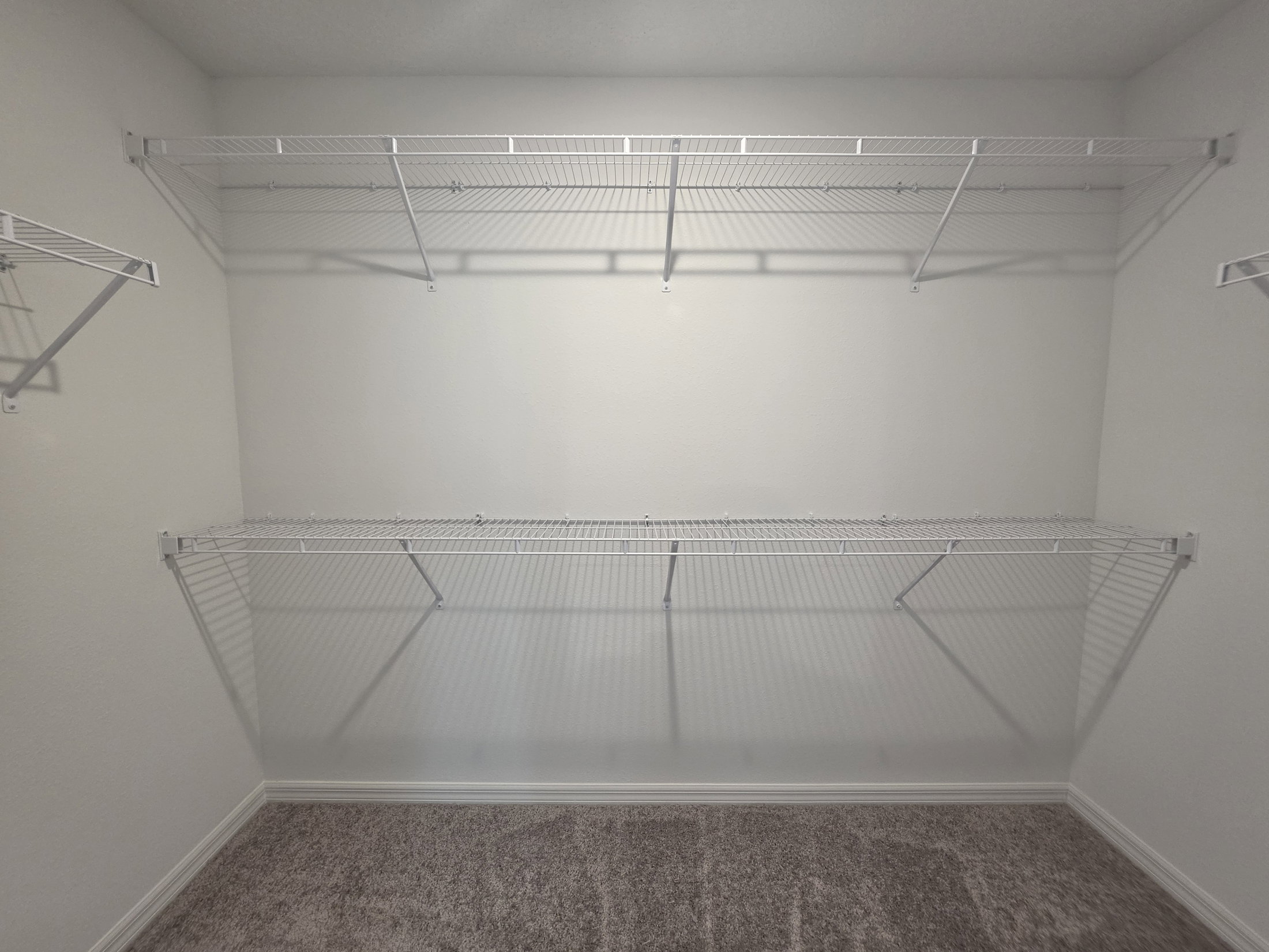 Empty closet with white wire shelving against a plain wall.