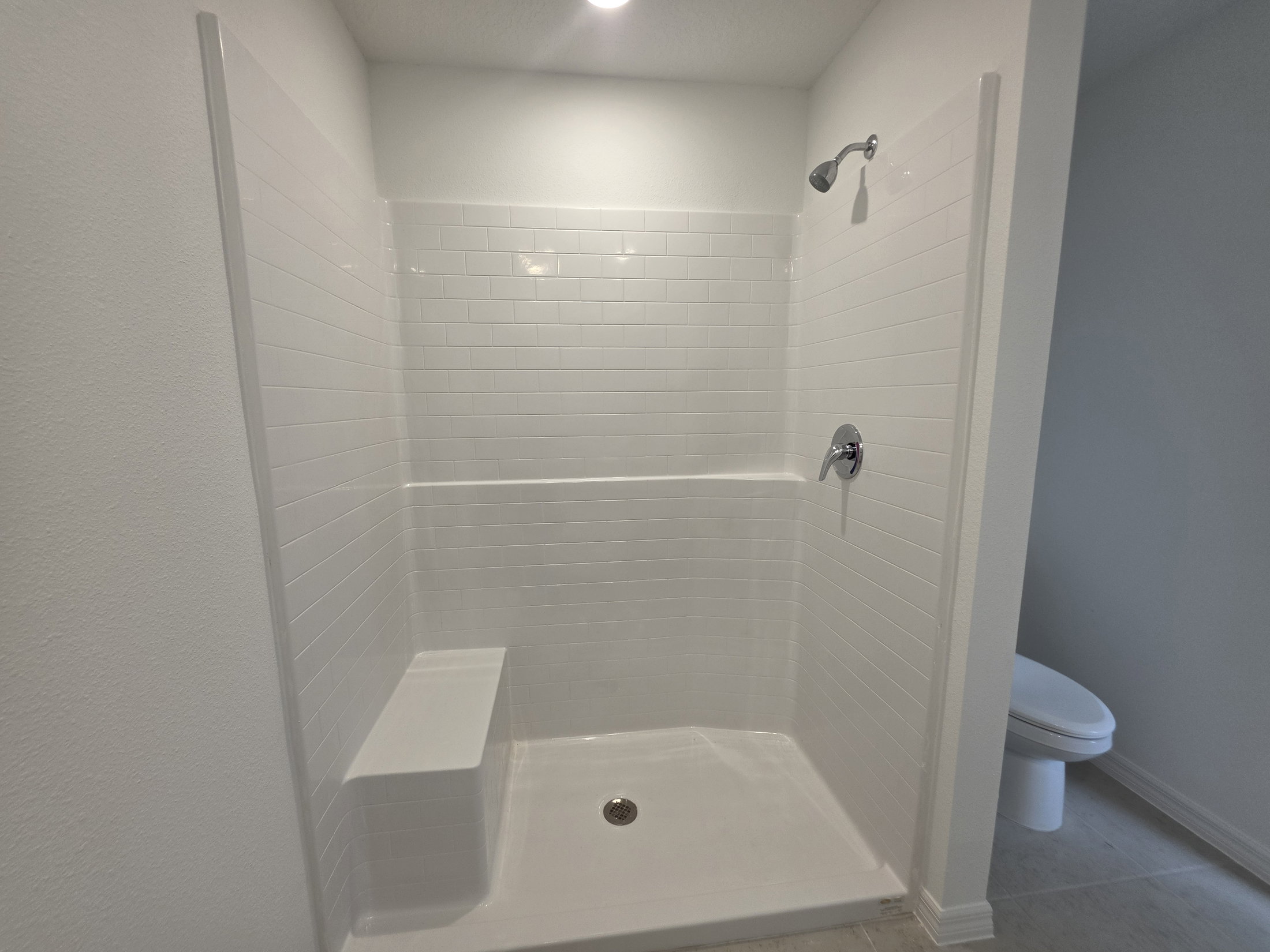A clean, white tiled shower with a built-in bench and modern fixtures in a bright, minimalistic bathroom.