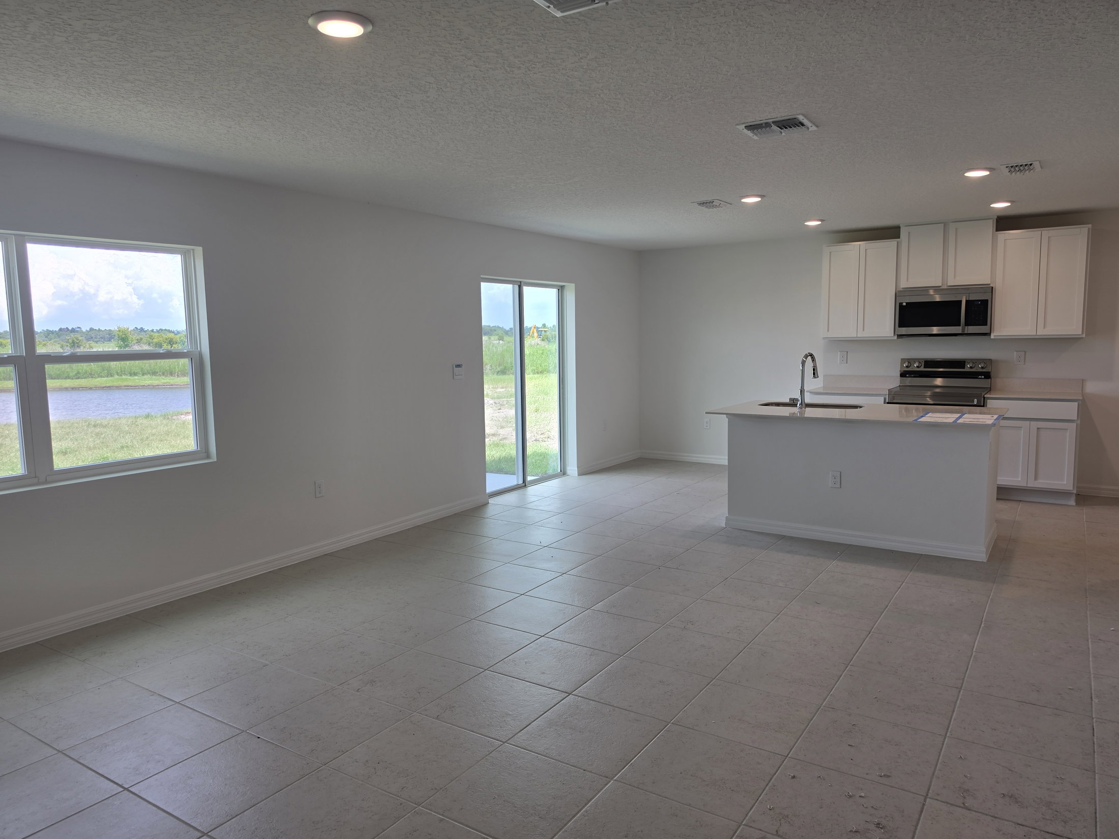 A spacious, modern kitchen and living area with tiled flooring, large windows, and access to an exterior patio.