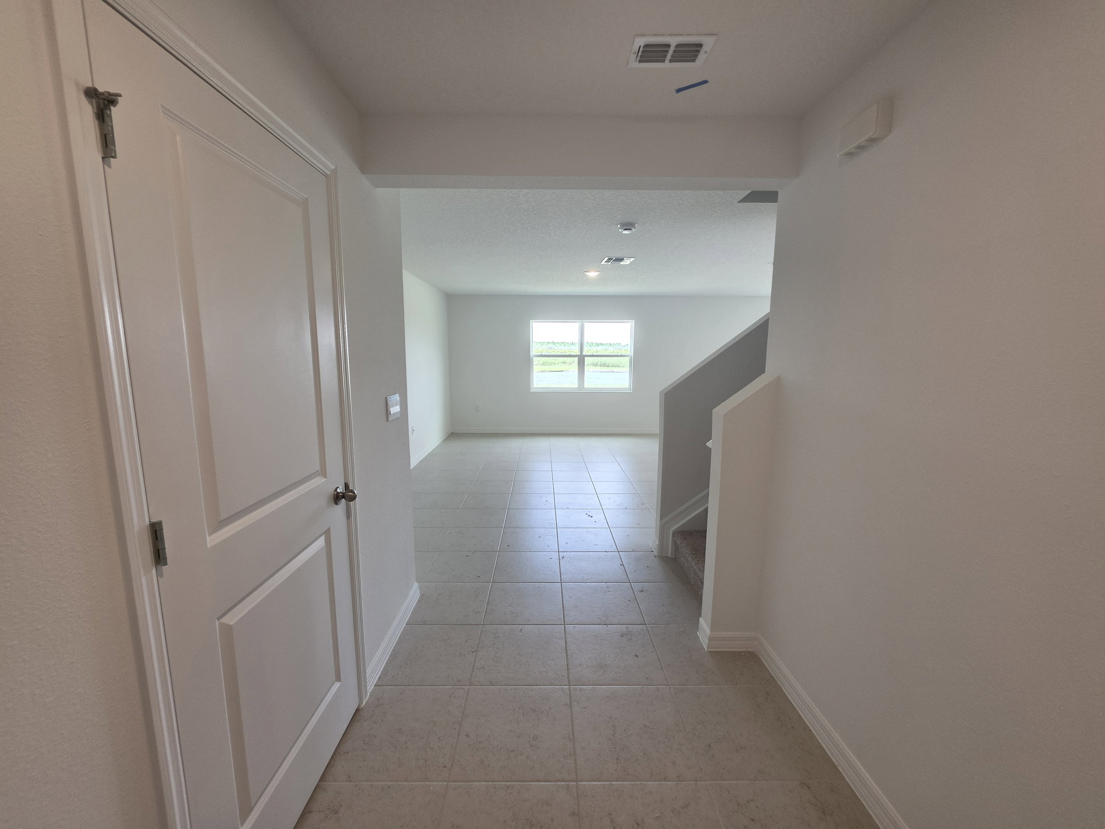 A hallway leading to a bright room with two windows and a staircase on the right.