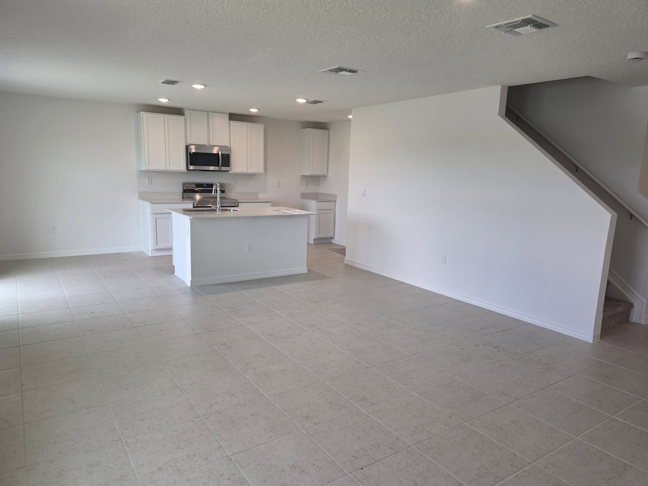 Open concept living area with a kitchen island, white cabinetry, and tiled floor.