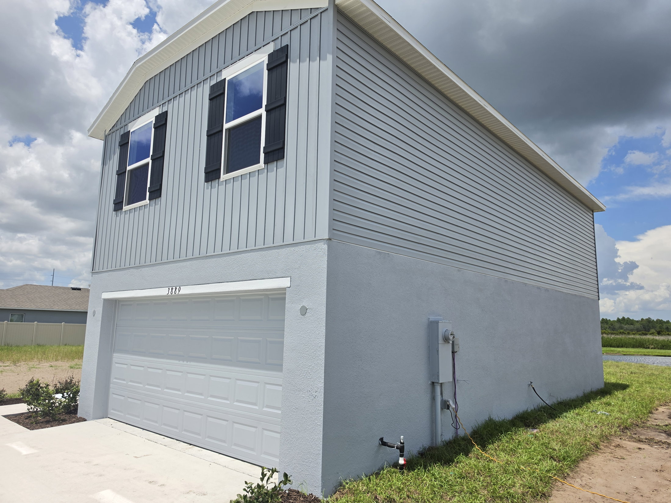 Two-story gray house with a garage, featuring white trim and black shutters under a partly cloudy sky.
