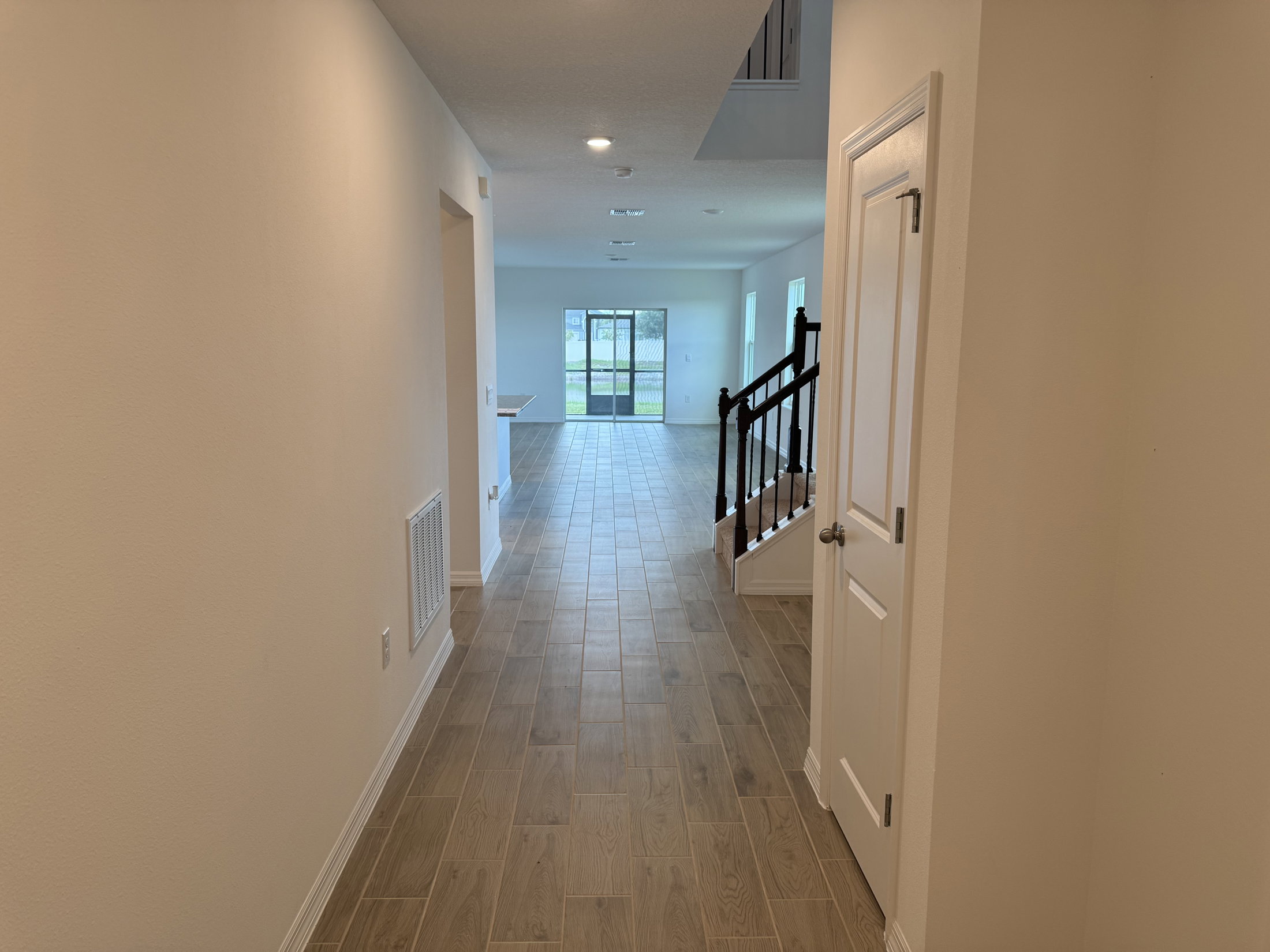 A spacious, well-lit hallway leading to an open living area with tile flooring and a staircase.