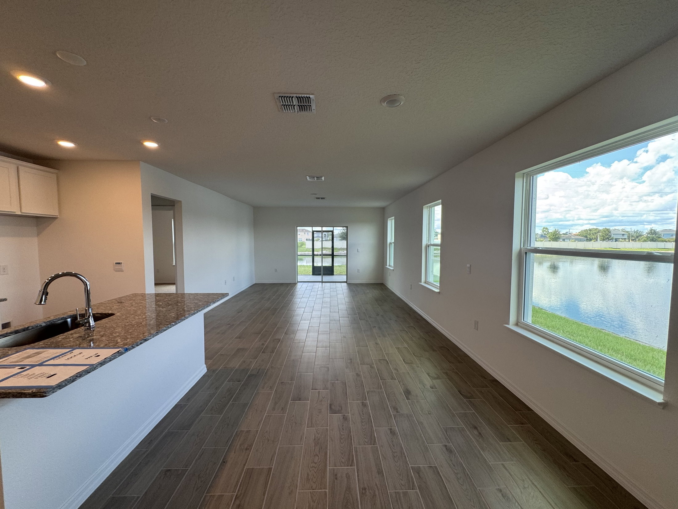 Spacious living area with tile flooring and large windows overlooking a pond.