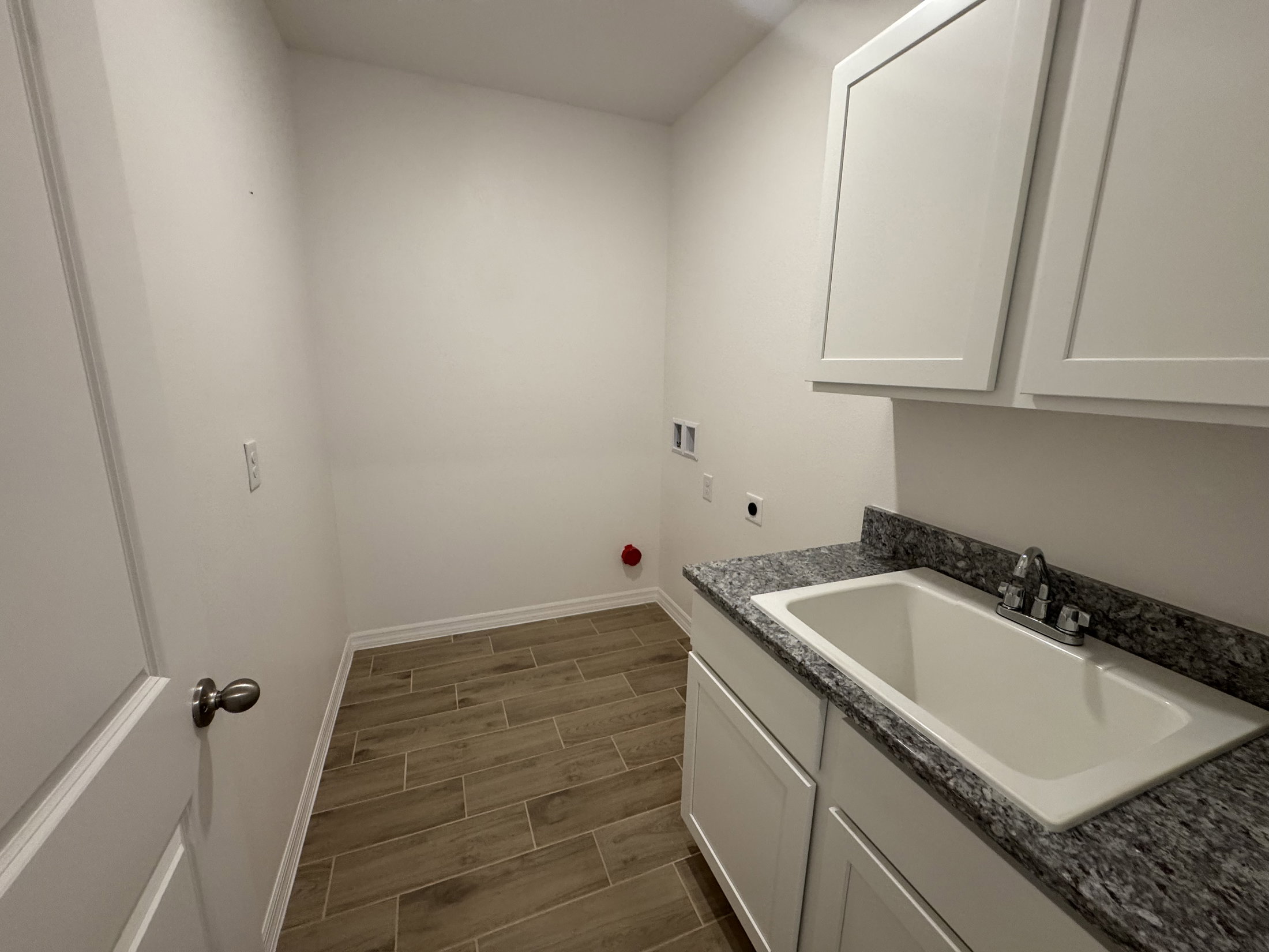 A clean, empty laundry room with white cabinets and a granite countertop.