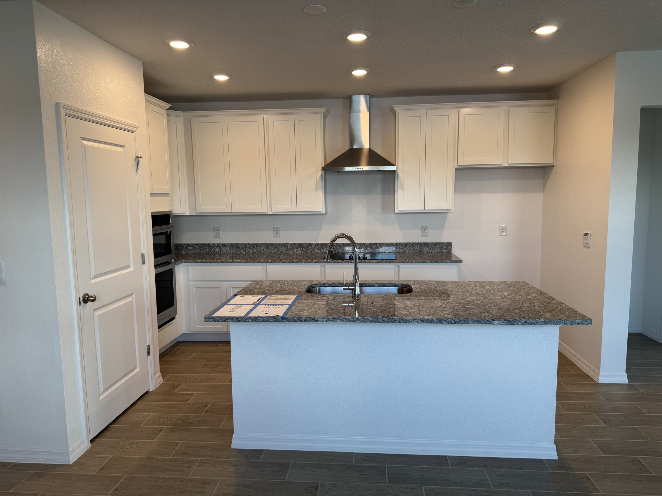 Modern kitchen featuring white cabinets, a stainless steel hood, granite countertops, and a central island with a sink.