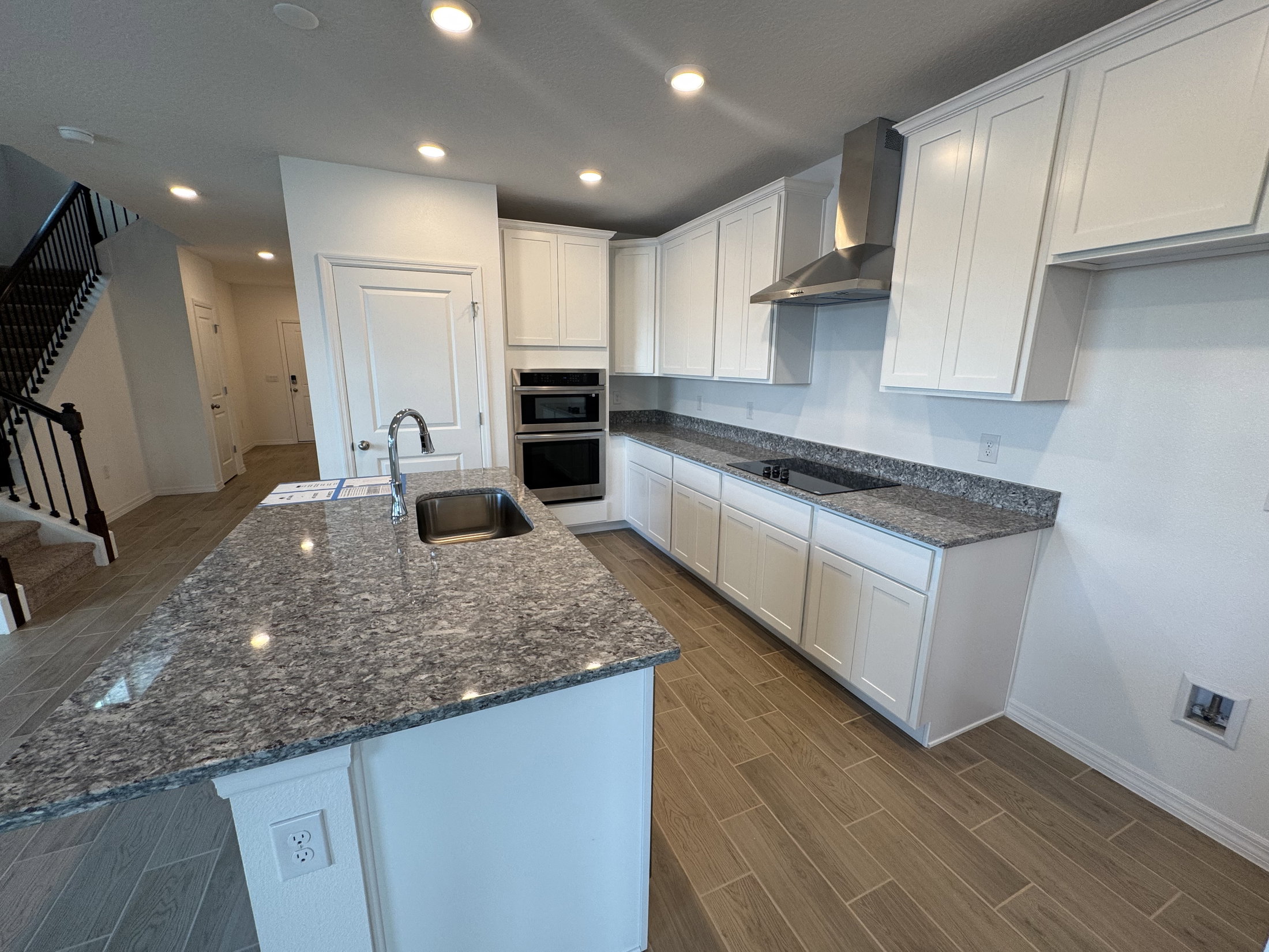Modern kitchen featuring white cabinetry, granite countertops, stainless steel appliances, and hardwood flooring.
