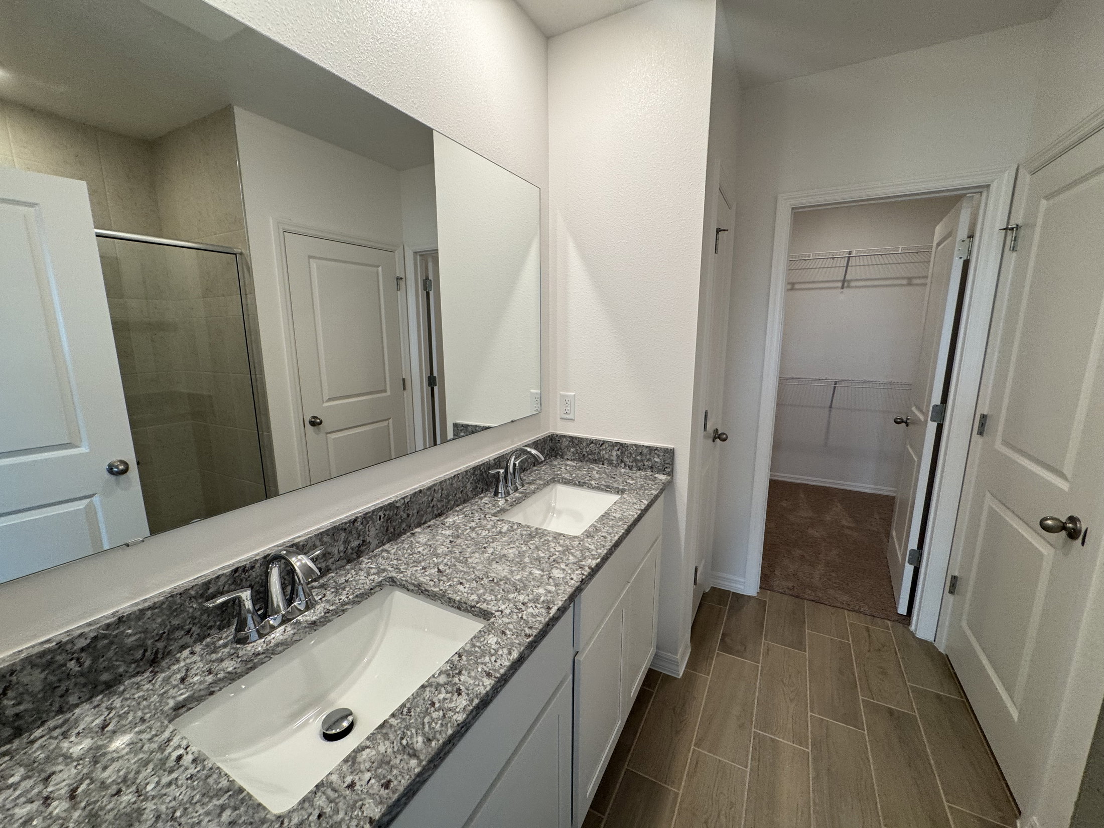 Modern bathroom with double sinks, granite countertop, and a large mirror, with an open closet visible in the background.
