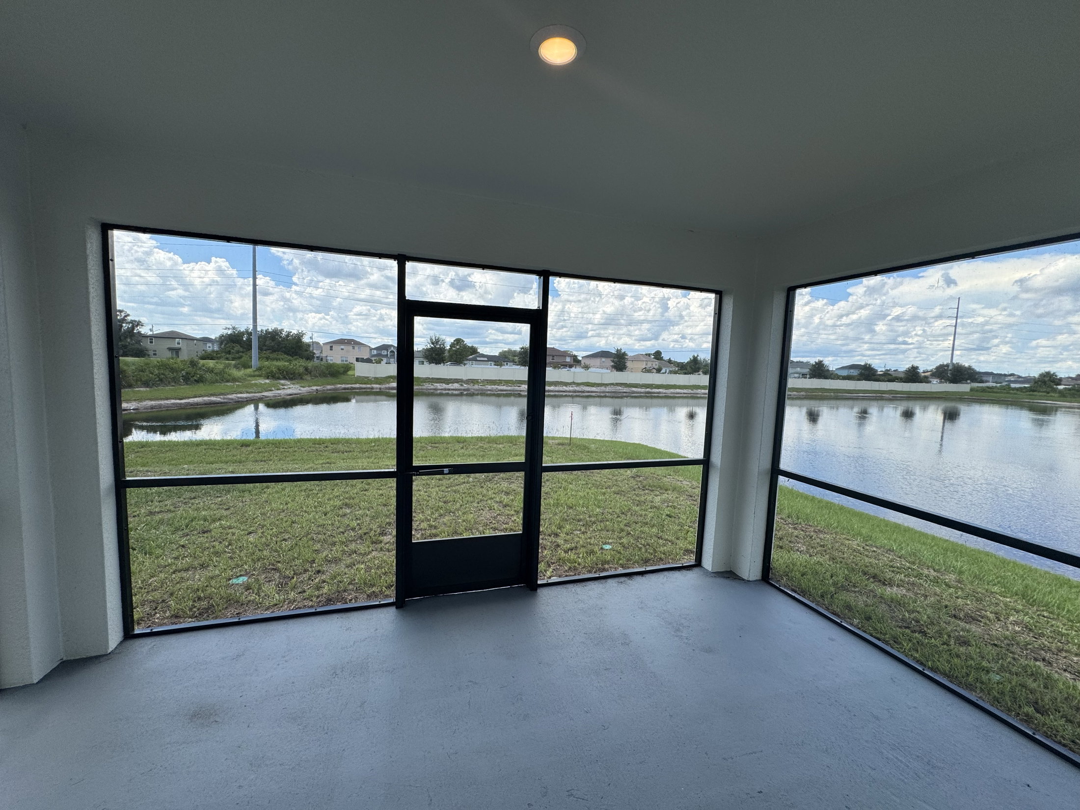 A screened-in porch overlooking a lake with grassy areas and cloudy skies.