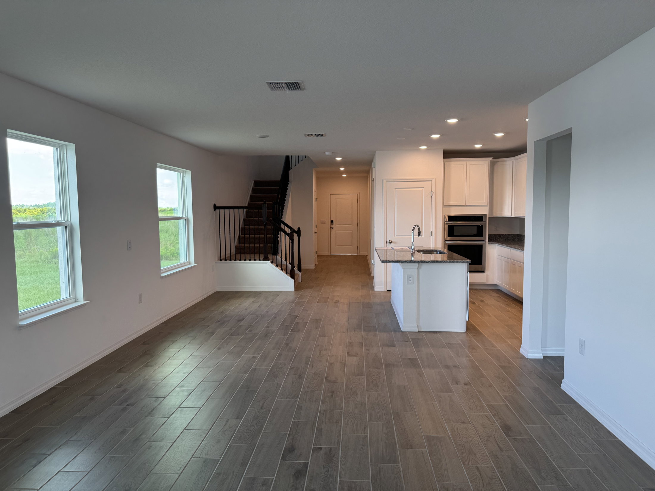 Spacious living area with a view of a staircase, kitchen, and large windows.