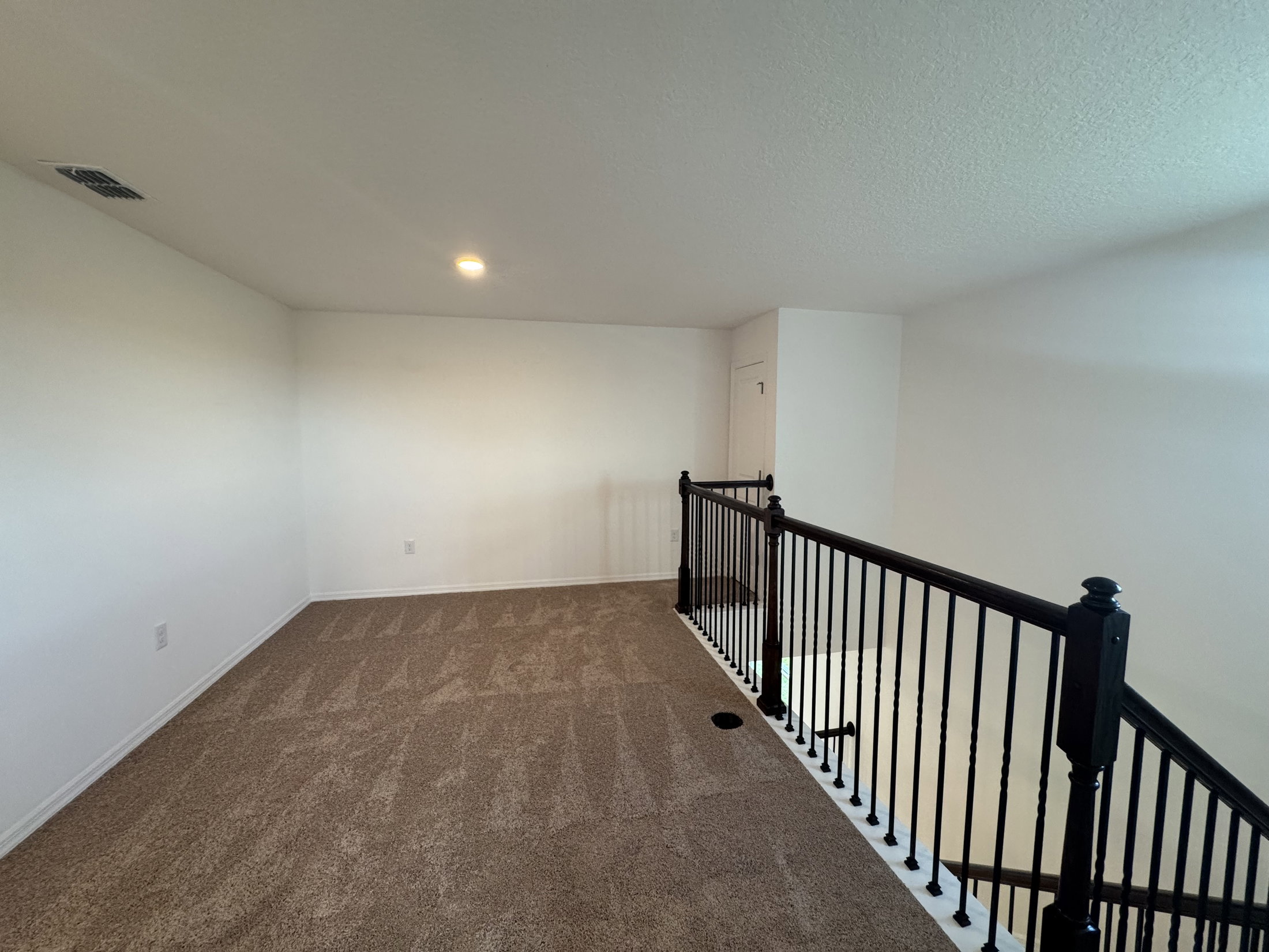 Spacious, carpeted landing area with a black railing overlooking a staircase.