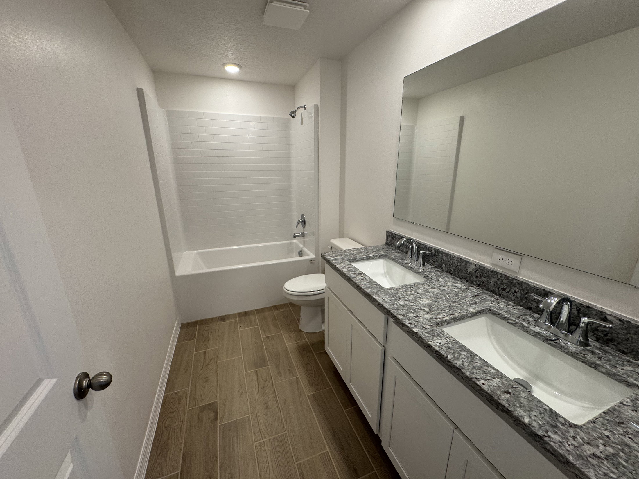 Spacious bathroom featuring a double vanity with granite countertops, a large mirror, and a bathtub with a shower.