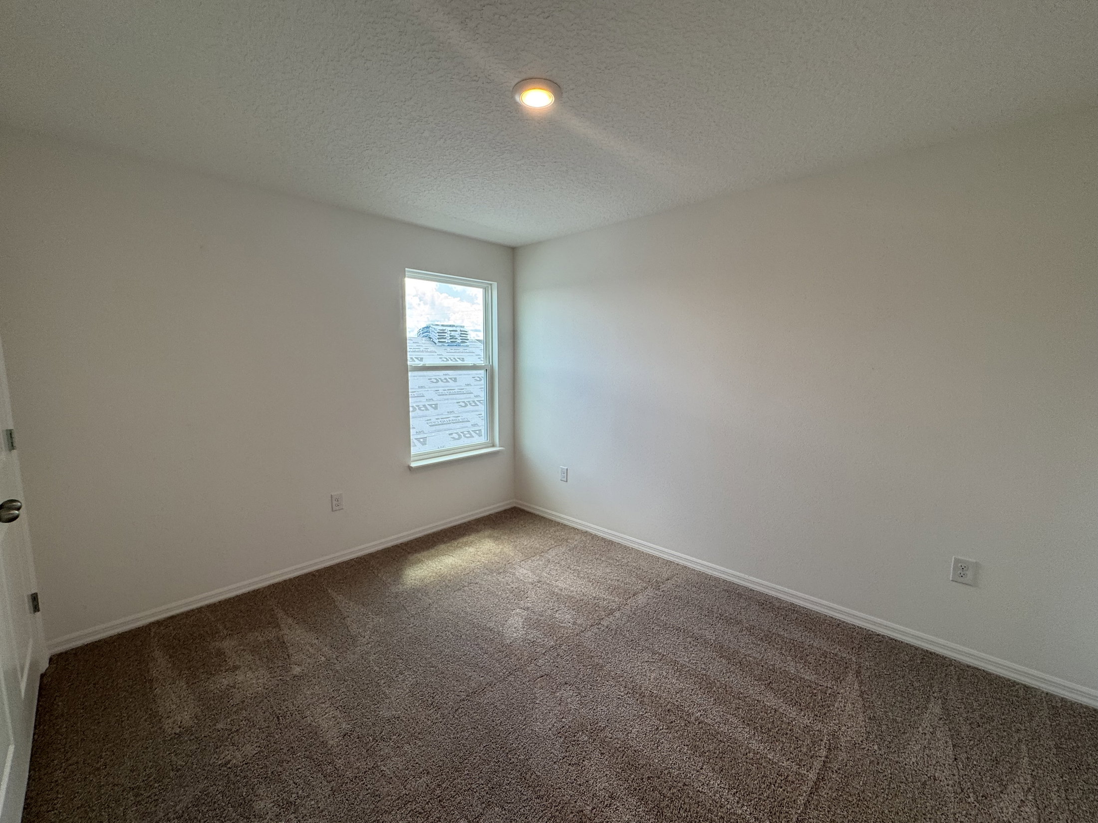 Empty room with beige carpet, a single window letting in natural light, and white walls.