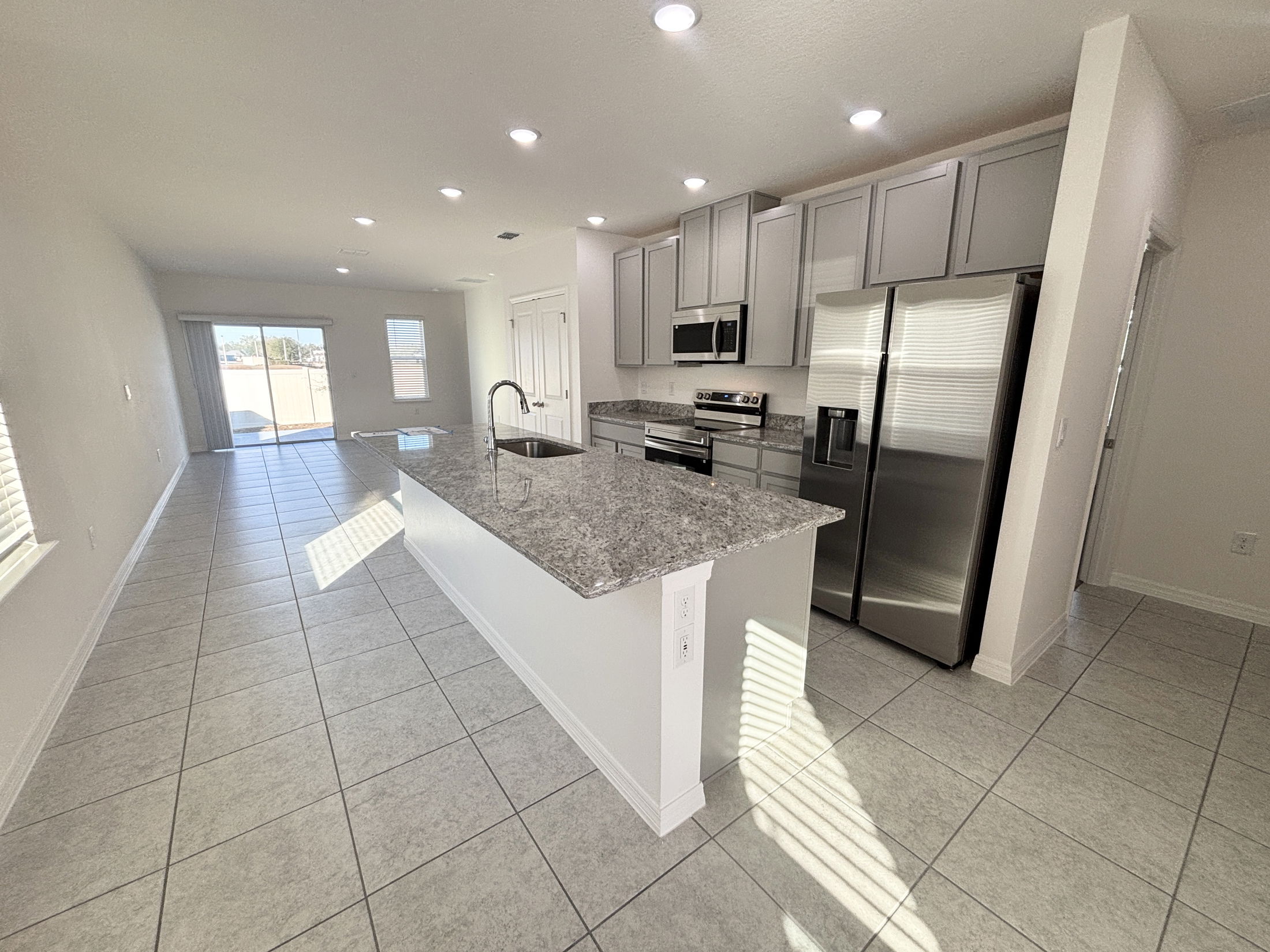 Modern kitchen and dining area with granite countertops, stainless steel appliances, and natural light through sliding glass doors.