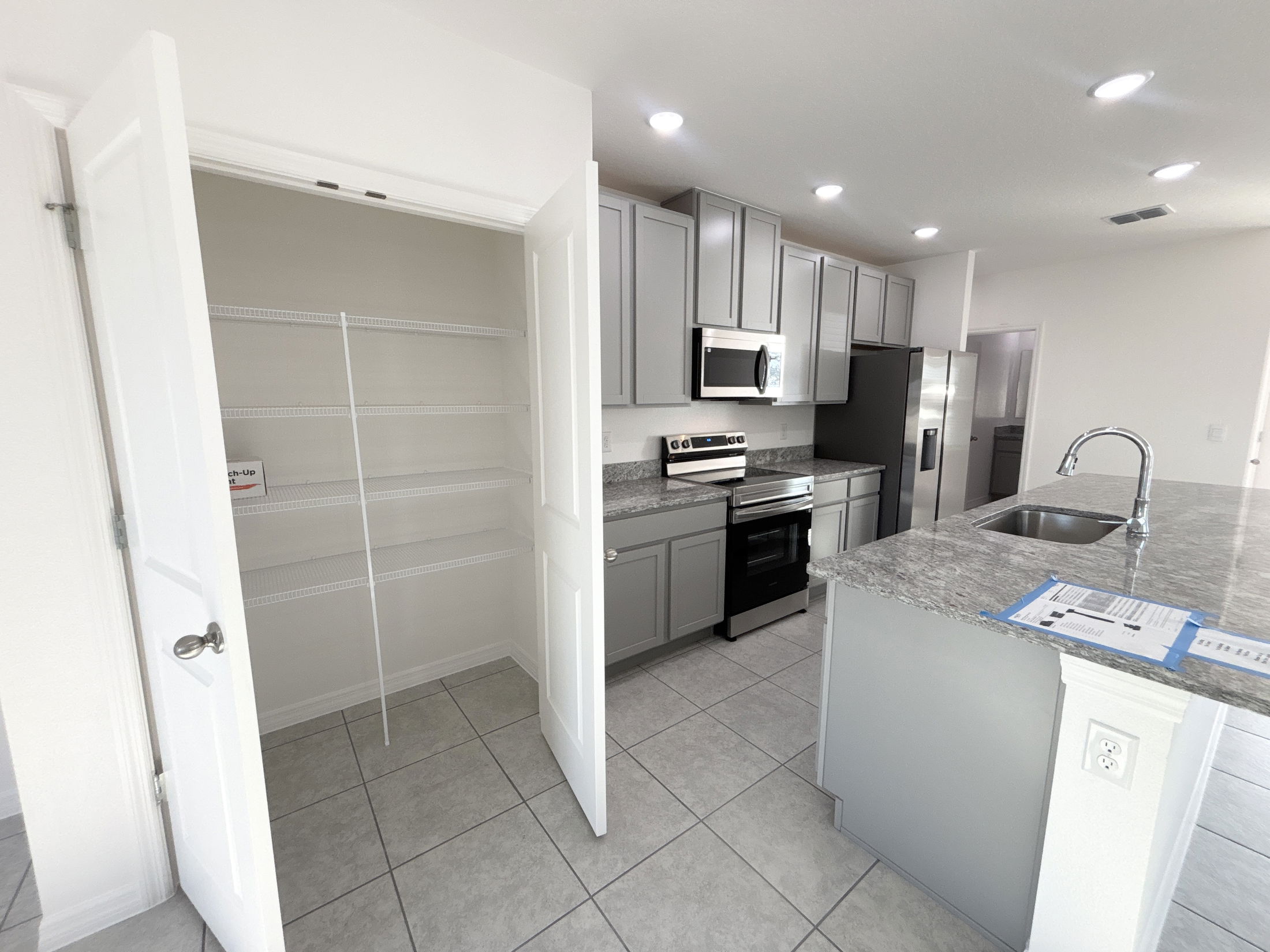 Modern kitchen interior featuring stainless steel appliances, gray cabinets, and an organized pantry with shelves.