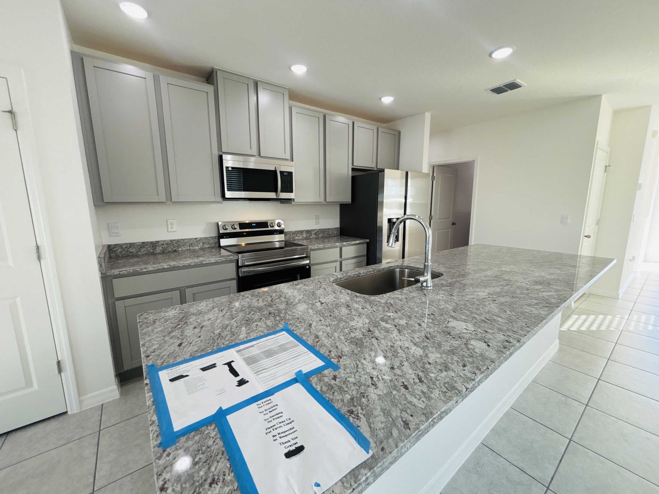 Modern kitchen with gray cabinets, stainless steel appliances, and granite countertops featuring a central island and natural light.
