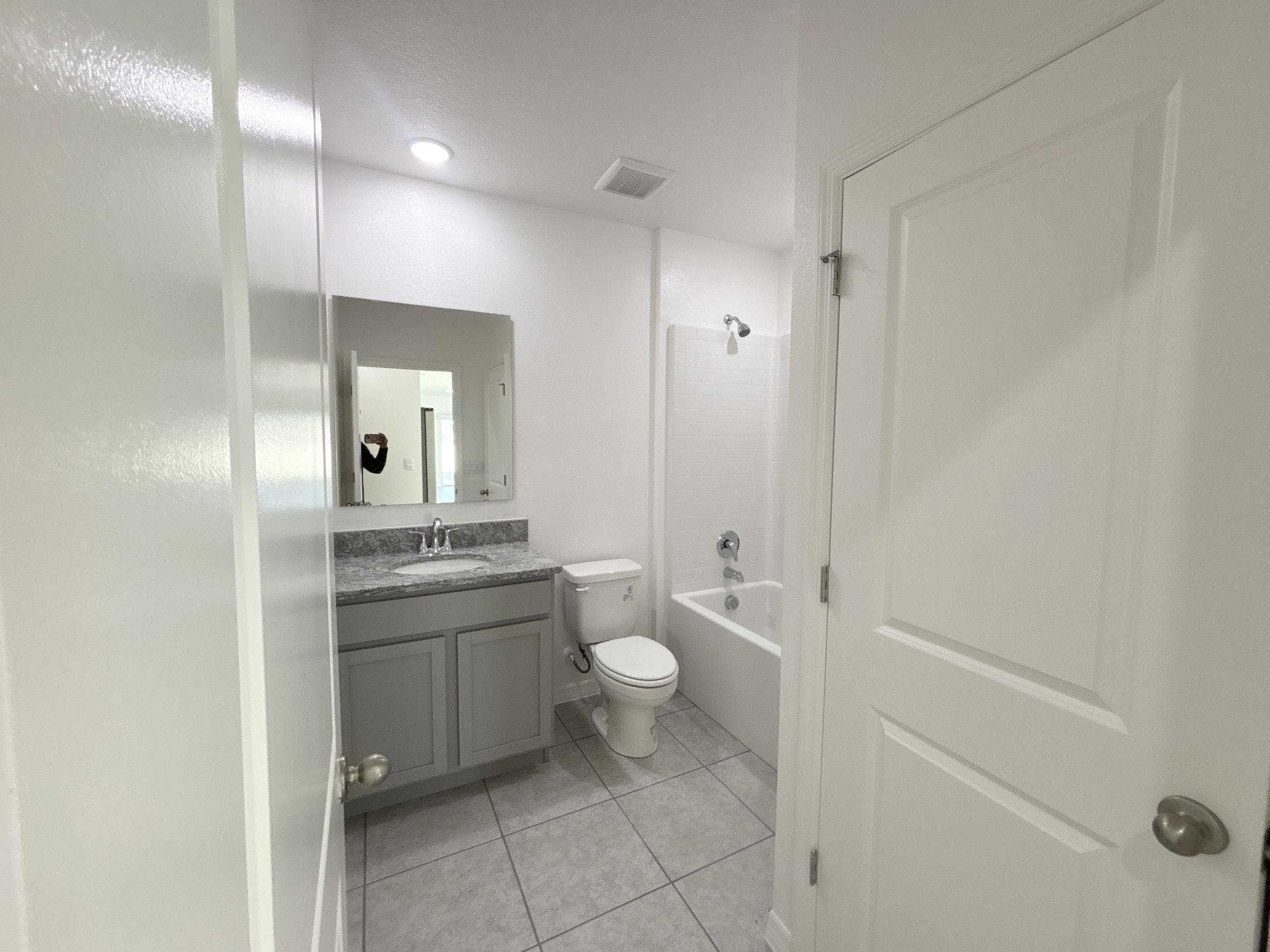 Modern bathroom with gray cabinetry, granite countertop, and bathtub in a bright, clean space.