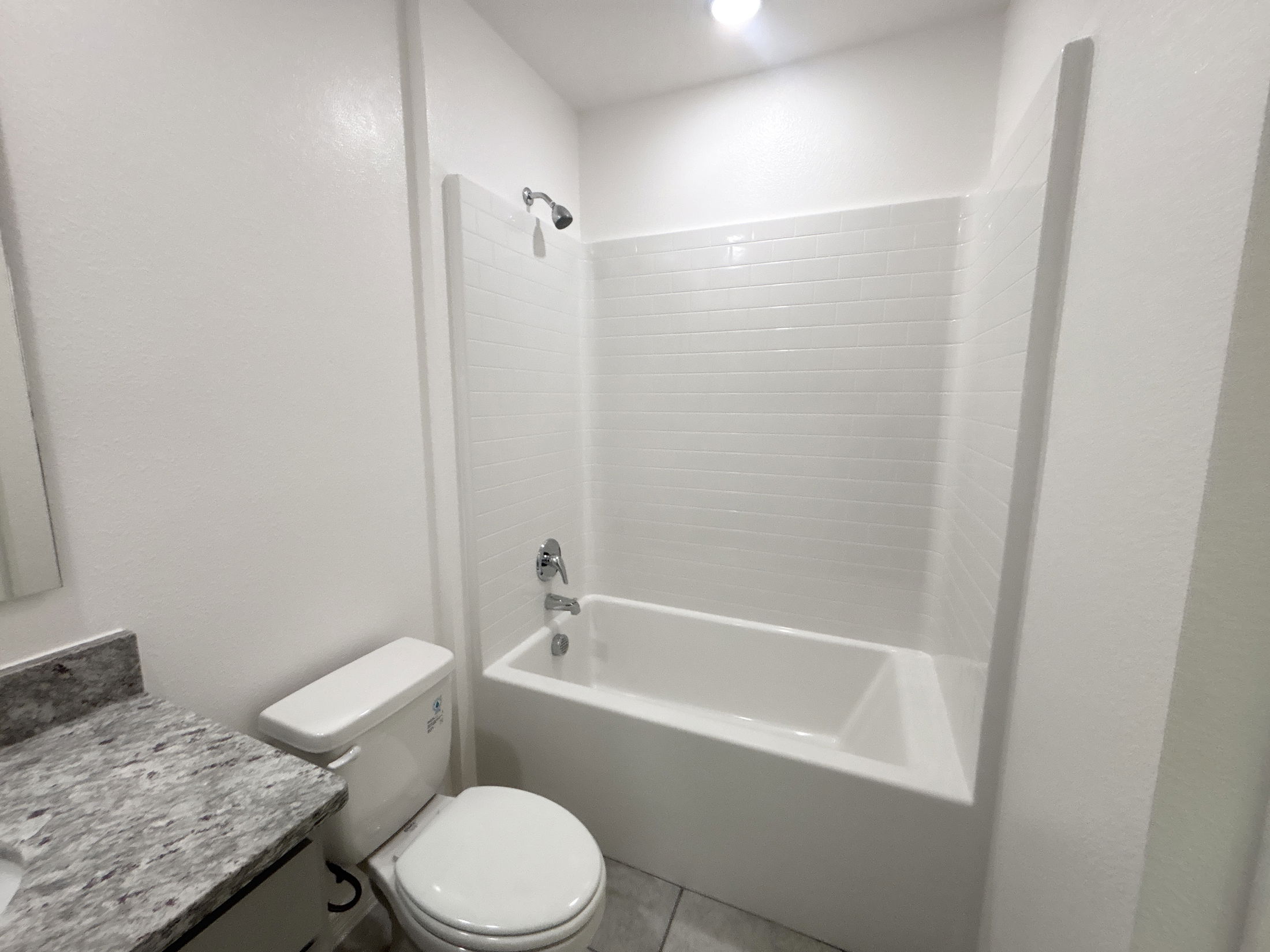 Modern bathroom featuring a shower-tub combo, tiled walls, and a sleek granite countertop.