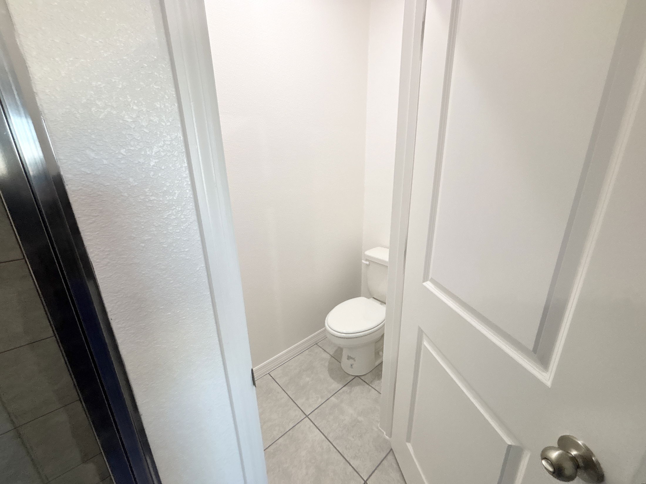 A clean and modern bathroom with a white toilet and light-colored tile flooring partially visible through an open door.