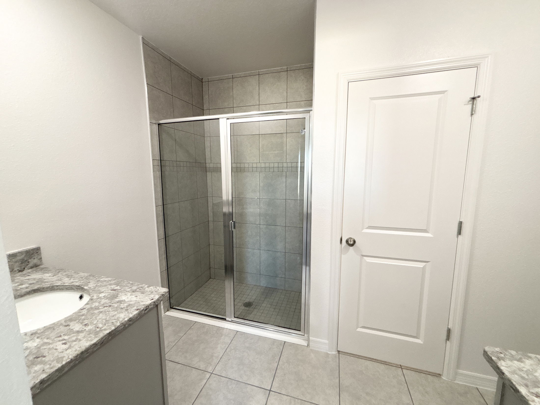 Modern bathroom featuring a glass-enclosed shower, granite countertops, and neutral tile flooring.