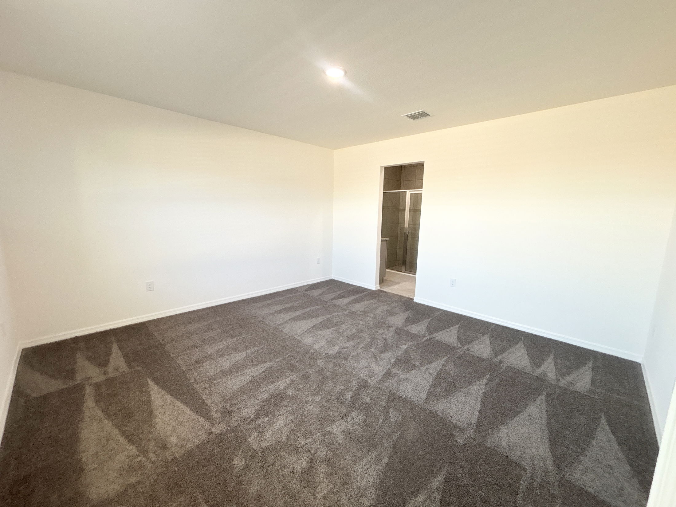 Spacious, empty bedroom with light gray carpet and a doorway leading to a bathroom.