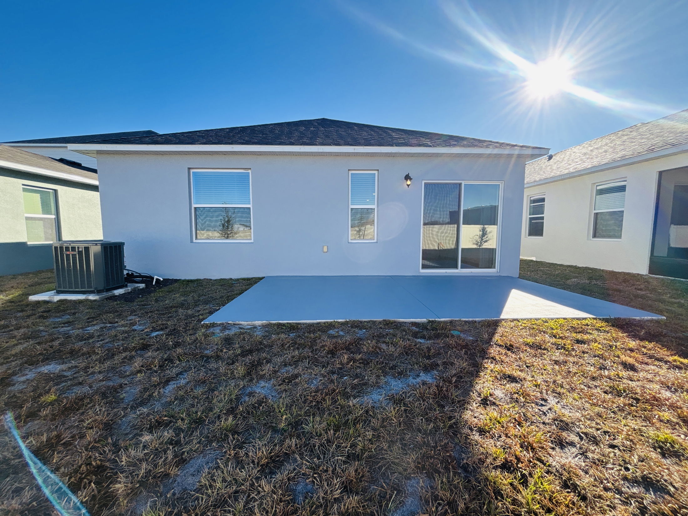 Backyard view of a modern home with a patio, air conditioning unit, and clear blue sky.