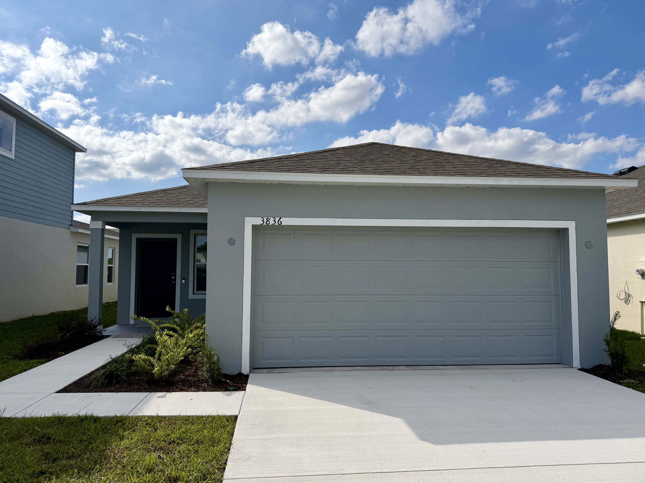 Modern single-story blue house with a double garage and a neatly landscaped front yard under a bright blue sky.