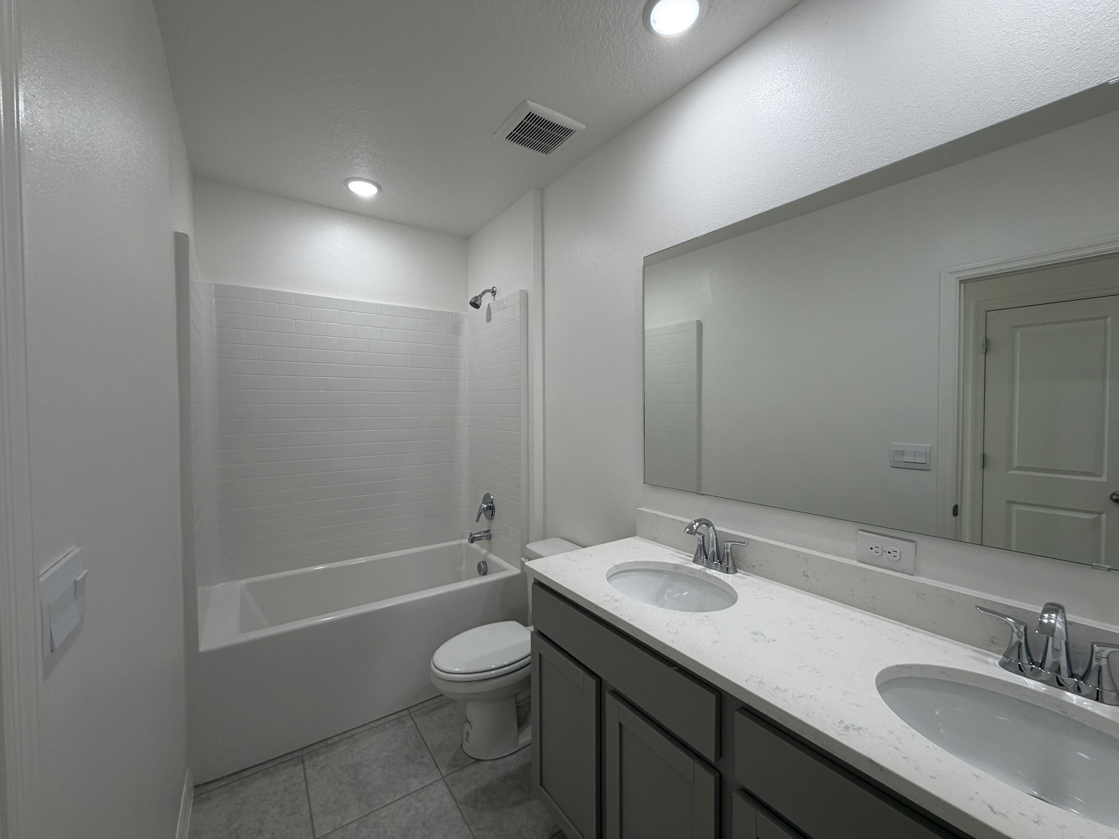 Modern bathroom with a double vanity, large mirror, and a white bathtub with a tile surround.